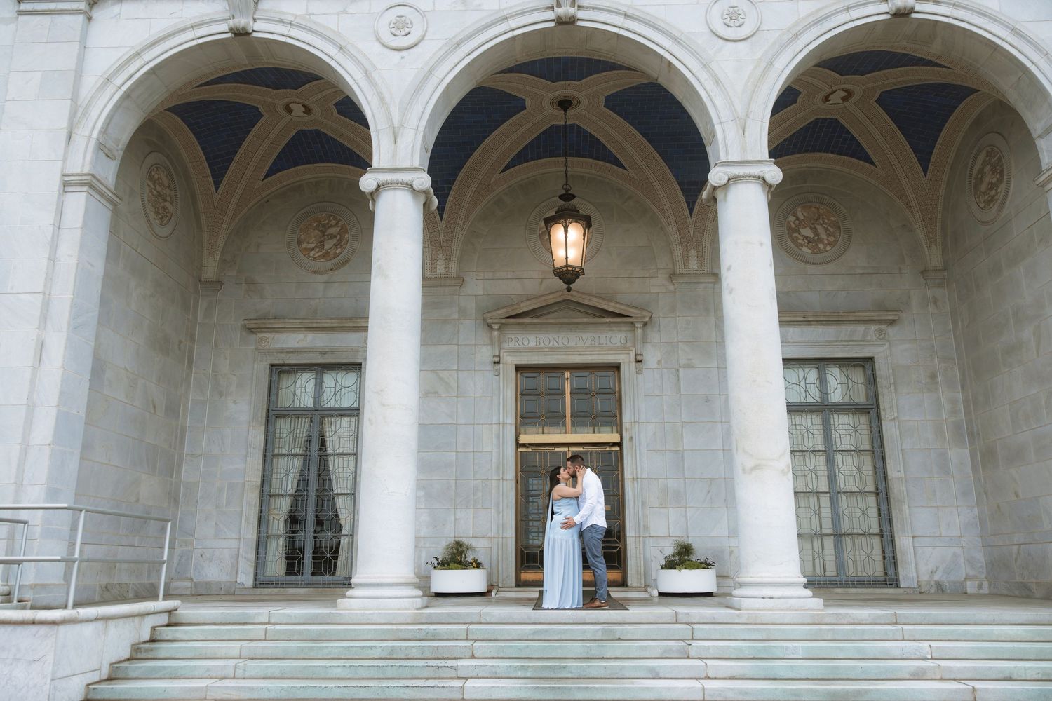 A couple shares a romantic moment under elegant stone archways of a grand historic building entrance.