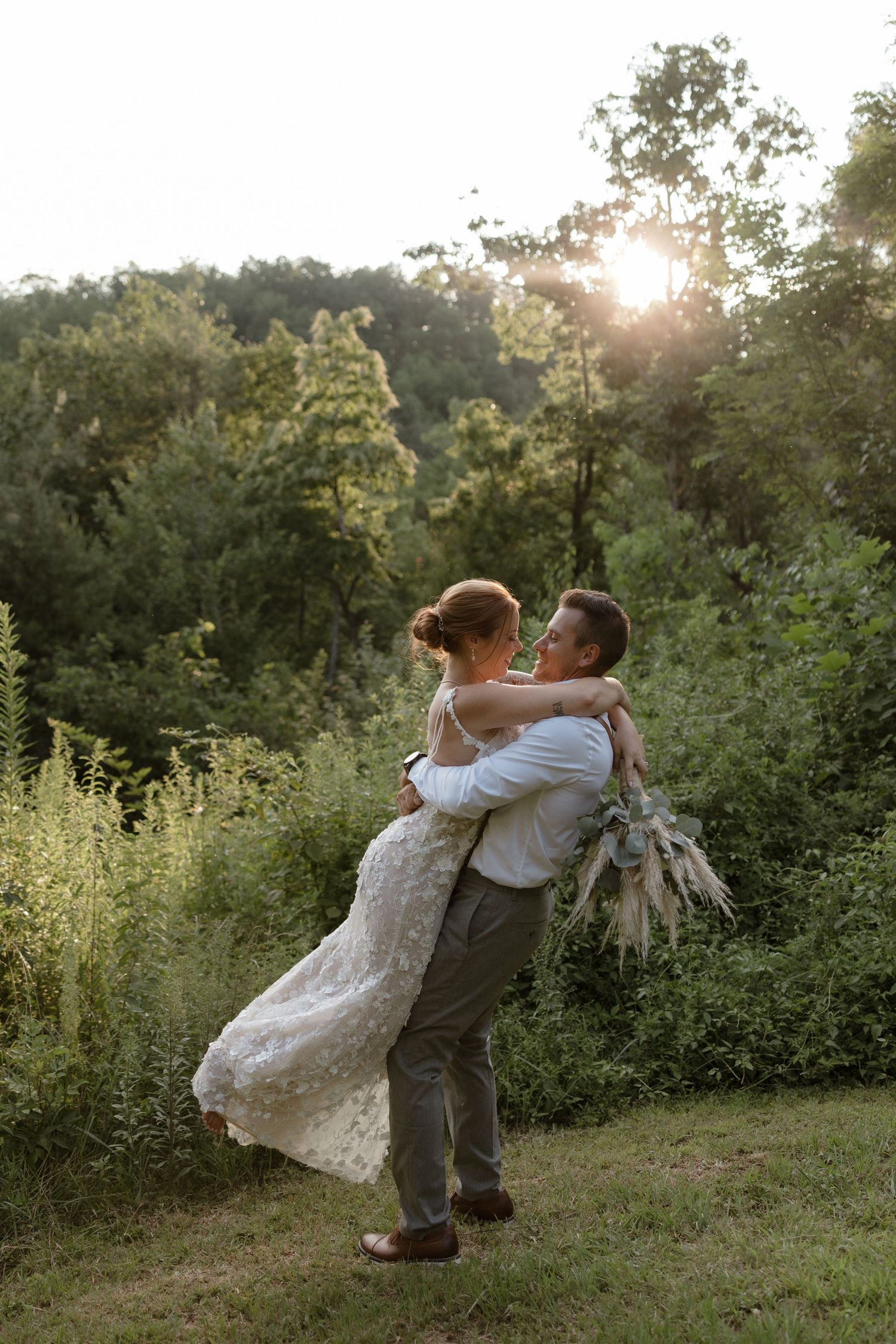 A romantic couple swings and embraces in a sunlit meadow during golden hour with lush greenery in the background.