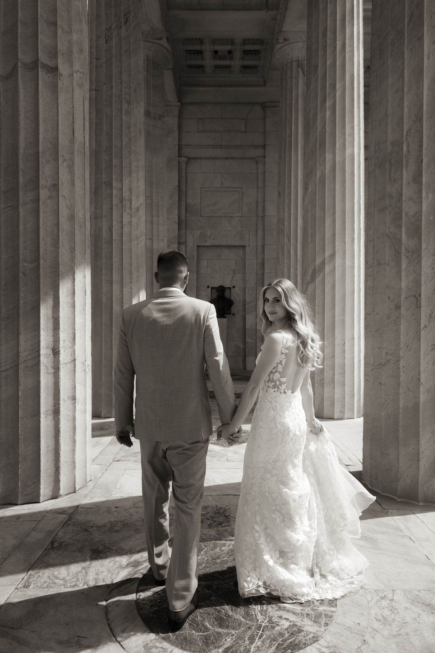 Artistic black and white wedding photos captured in a columned walkway with dramatic lighting.