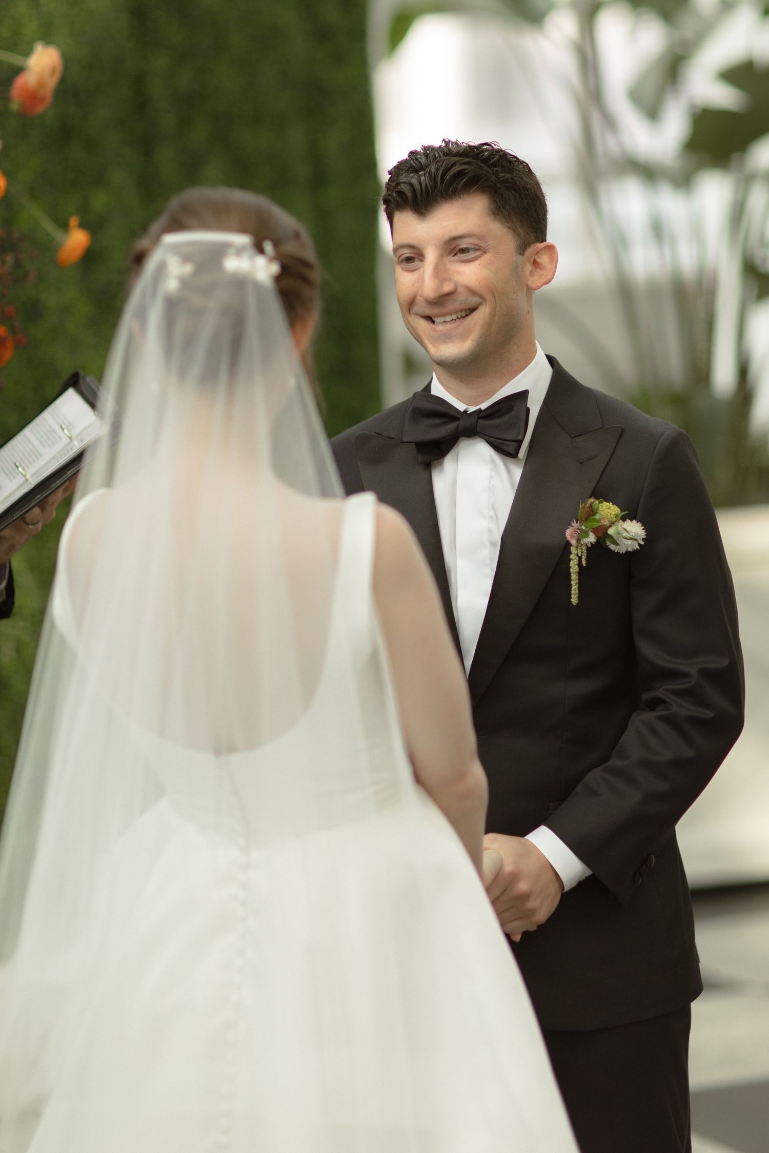 Wedding ceremony moment at a greenhouse venue decorated with orange and white florals.