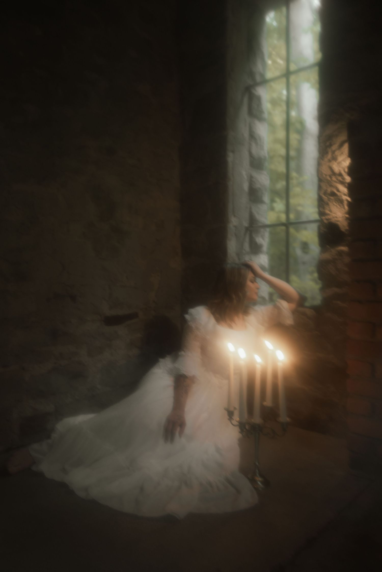A dreamy scene of a person in a white wedding dress sitting near candlelight by a window in a dark stone room.