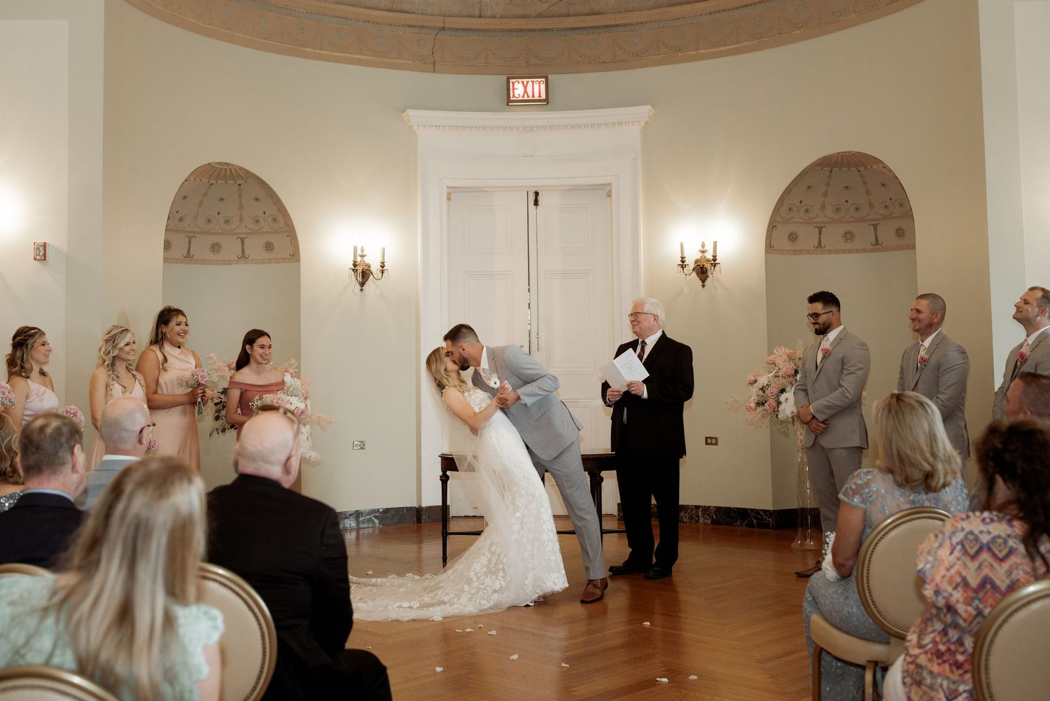 An elegant wedding ceremony takes place in a classic white room with arched details and wall sconces.
