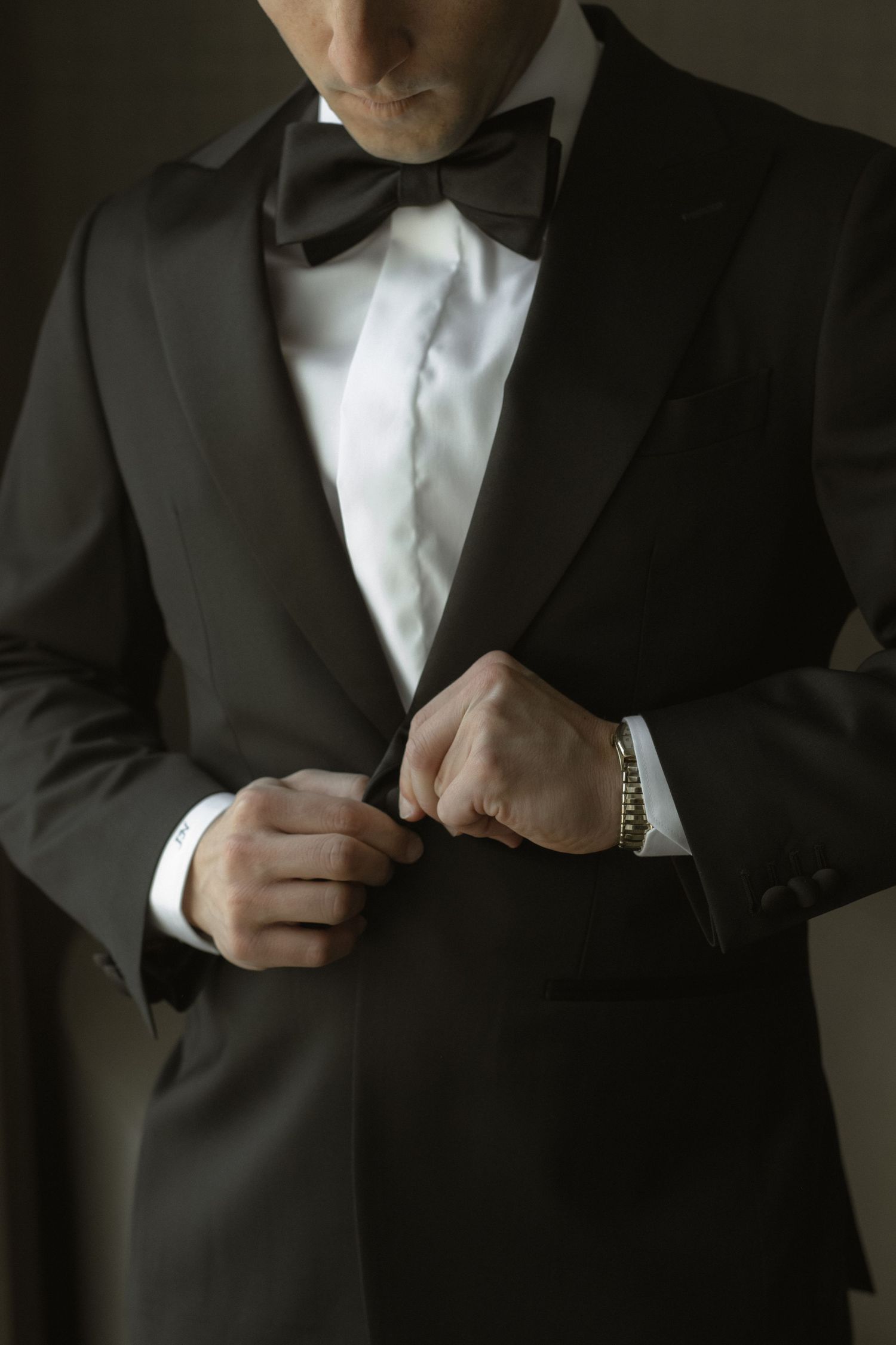 Close-up of hands adjusting a black bowtie on a classic tuxedo.