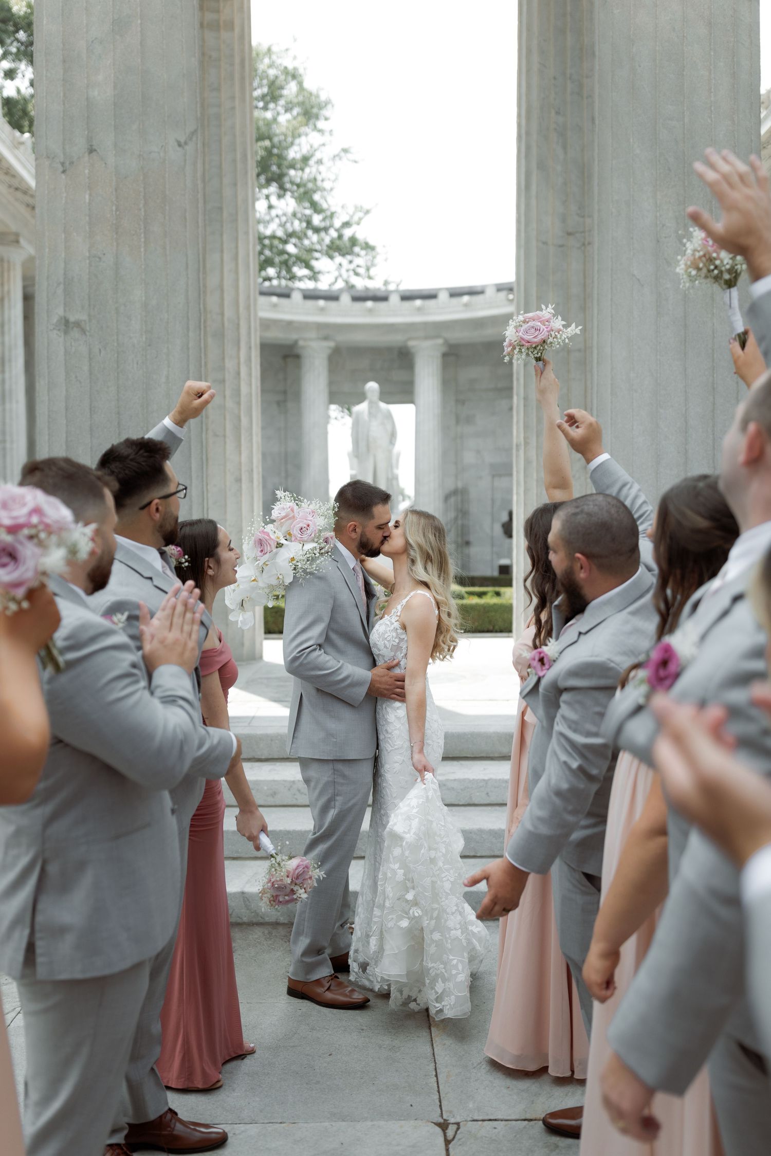Wedding celebration at a columned memorial with guests celebrating in grey and pink attire.