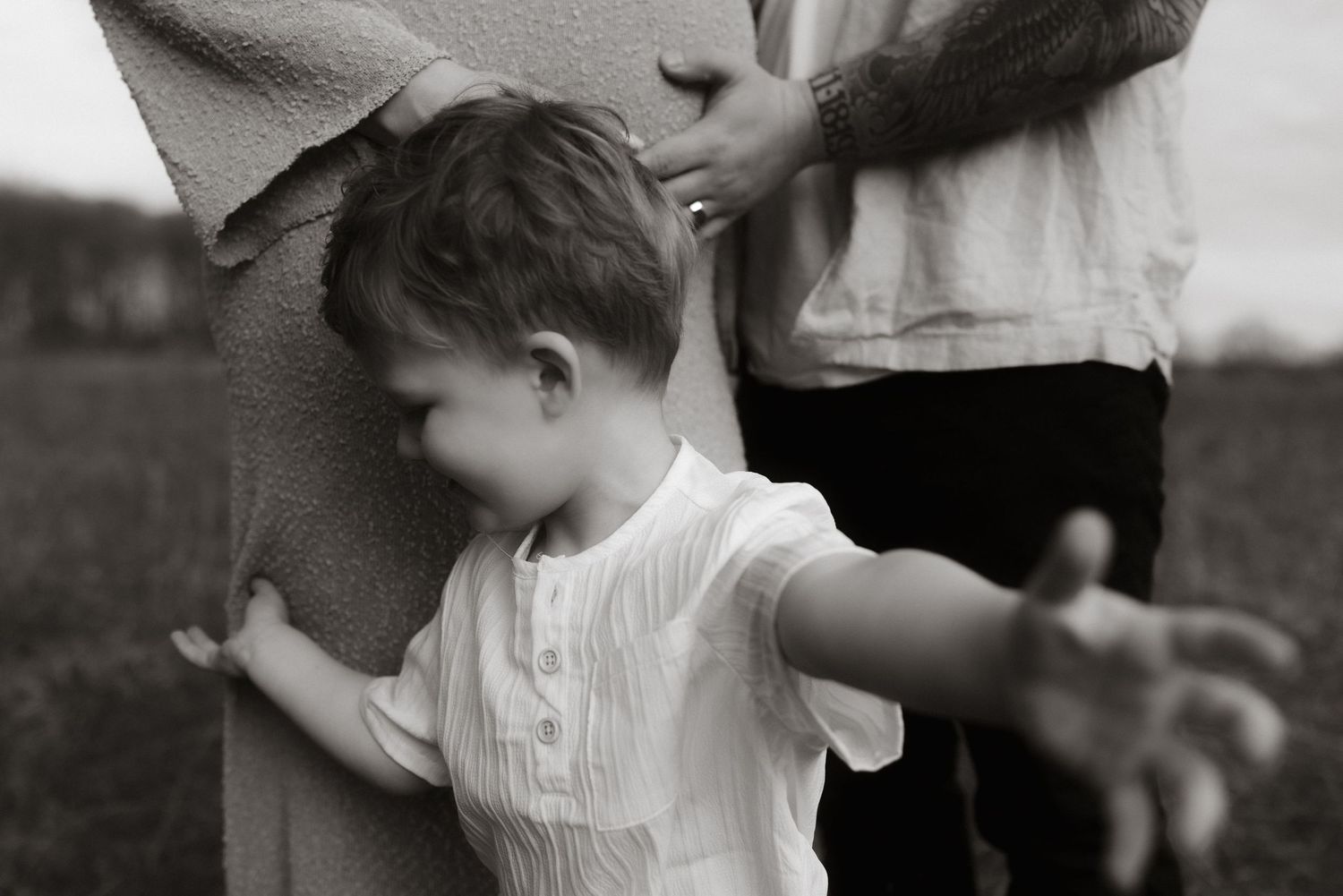 Child in white shirt reaching towards someone while playing hide and seek in black and white photo.