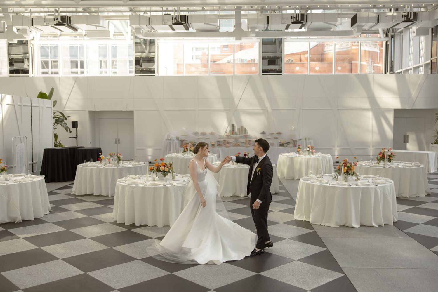 Elegant wedding reception venue with black and white checkered floor and round tables decorated in white linens.