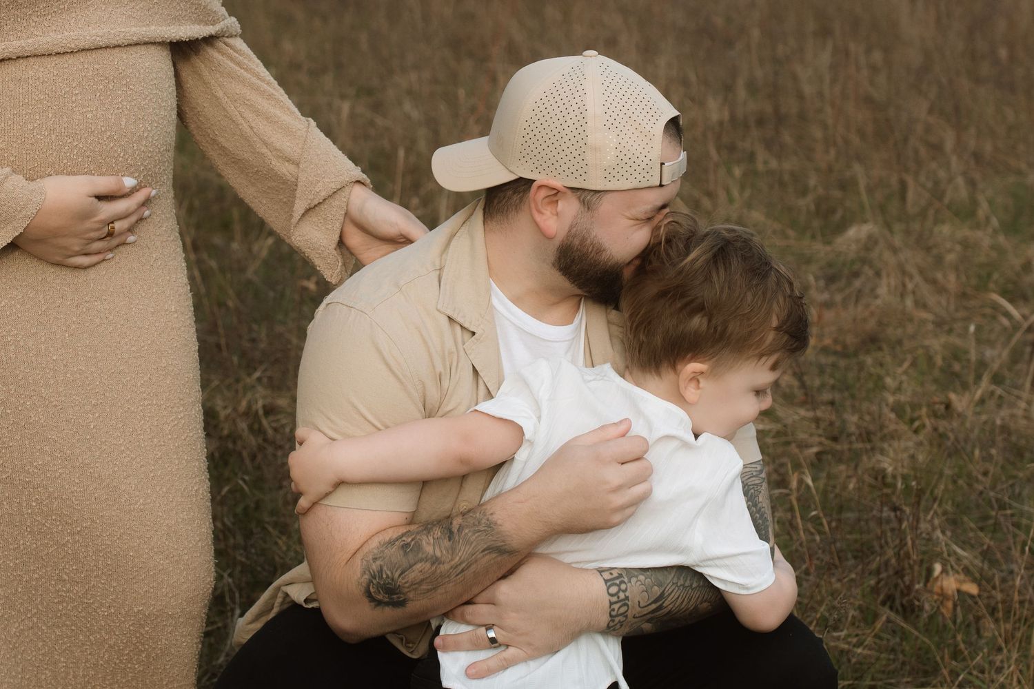 Family moment captured outdoors with toddler in white shirt and beige surroundings.
