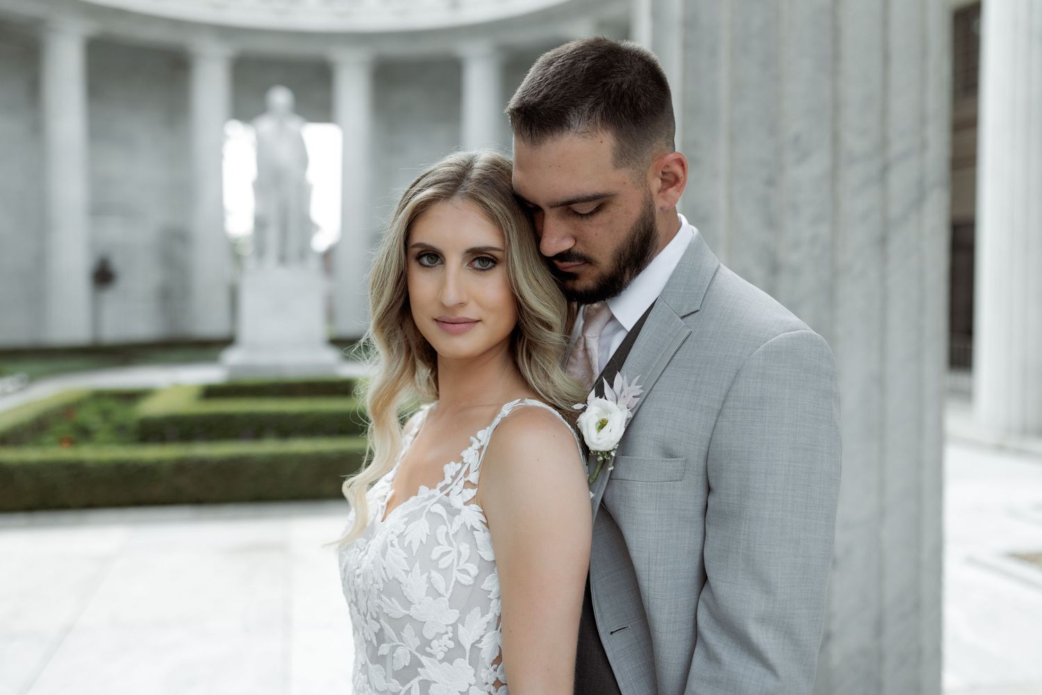 Elegant wedding portrait against white columned architecture with manicured garden in background.