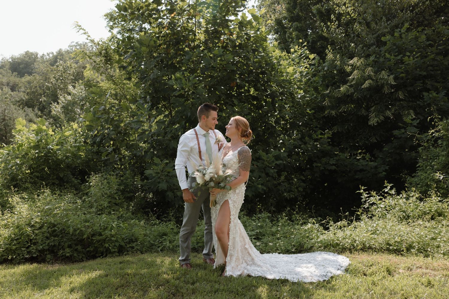 A romantic wedding couple embraces in a sunlit garden with lush green foliage in the background.