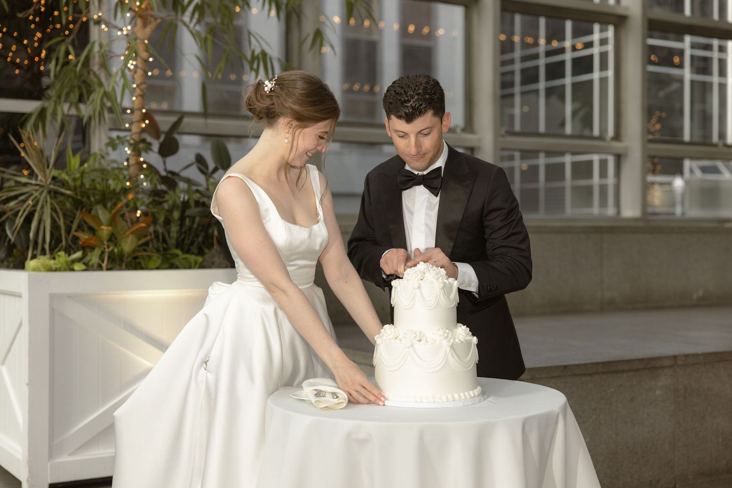 Couple cutting their elegant white wedding cake together at modern venue reception.