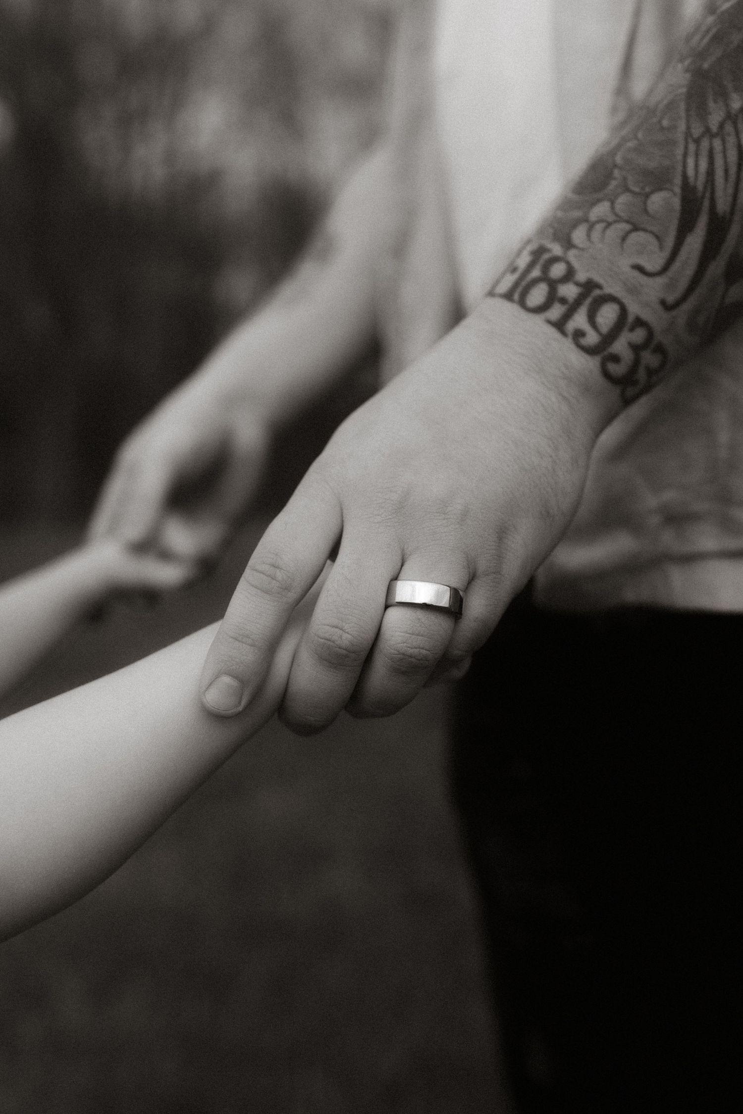 Close-up of a tattooed hand wearing a wedding band while holding another hand.