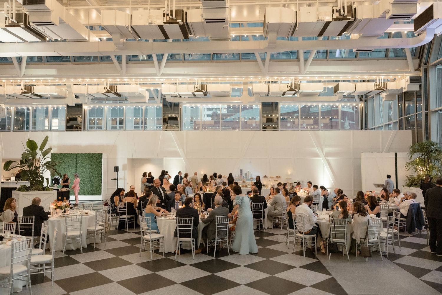 Modern wedding reception venue with checkerboard floor and guests seated at round tables.