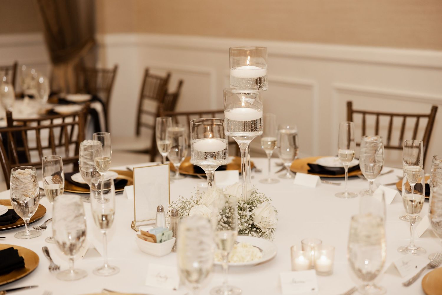 An elegant wedding reception table setting with floating candle centerpieces, wine glasses, and navy blue accents.