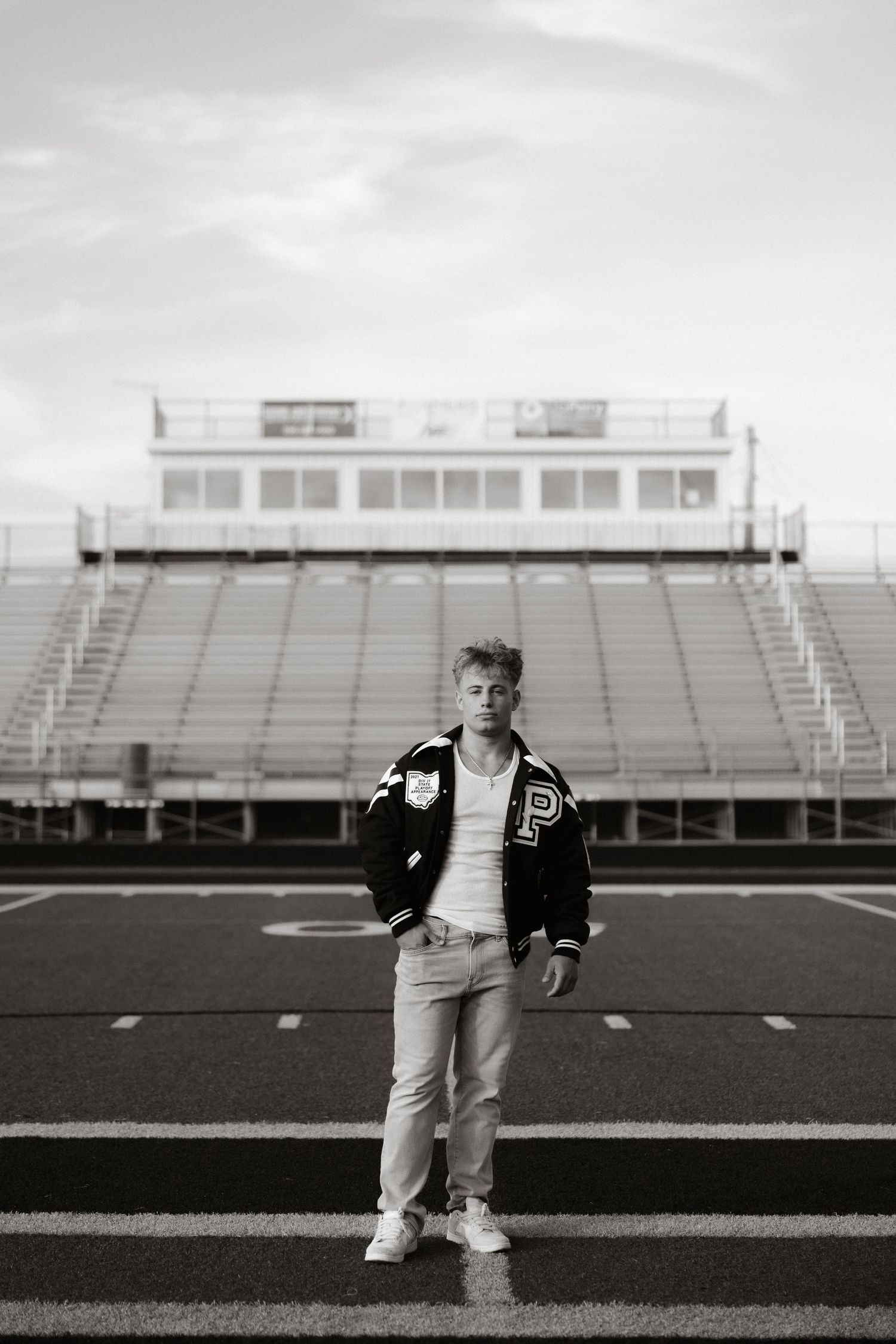 Black and white photo series of someone in varsity jacket posing on empty football stadium field.
