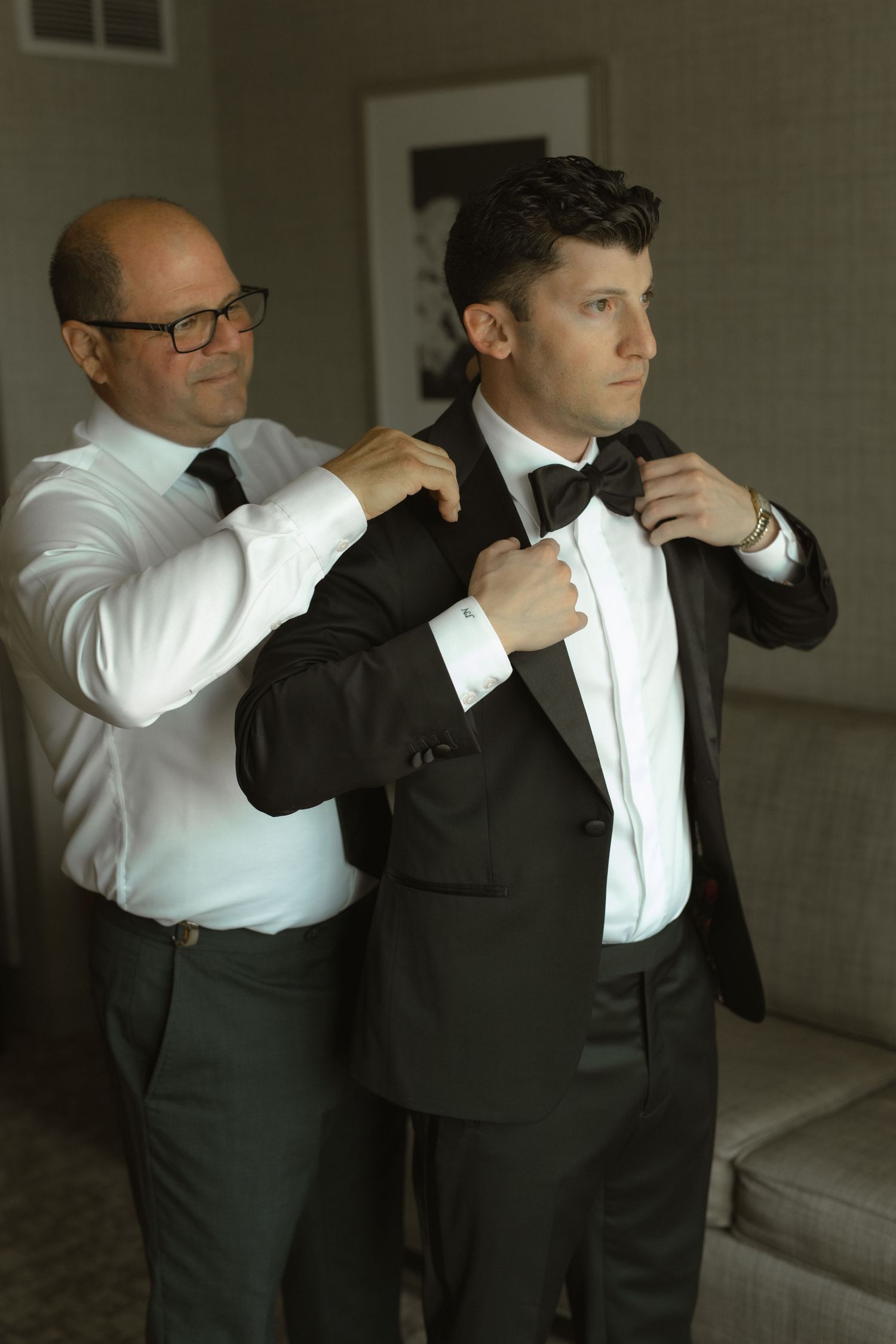 Two people in formal wear making final adjustments to a bowtie and tuxedo.