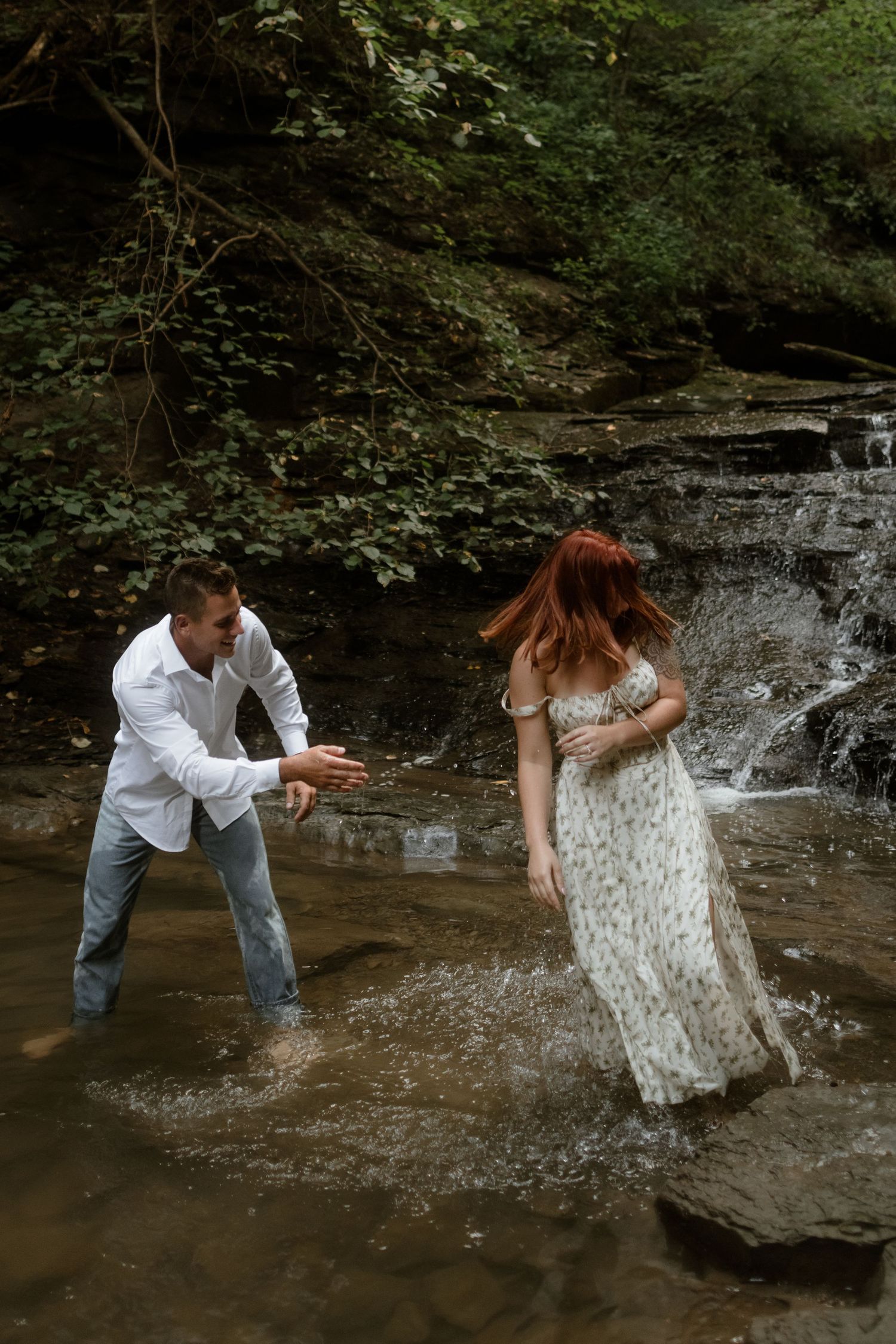 A couple splashes and plays together in a shallow forest waterfall stream.