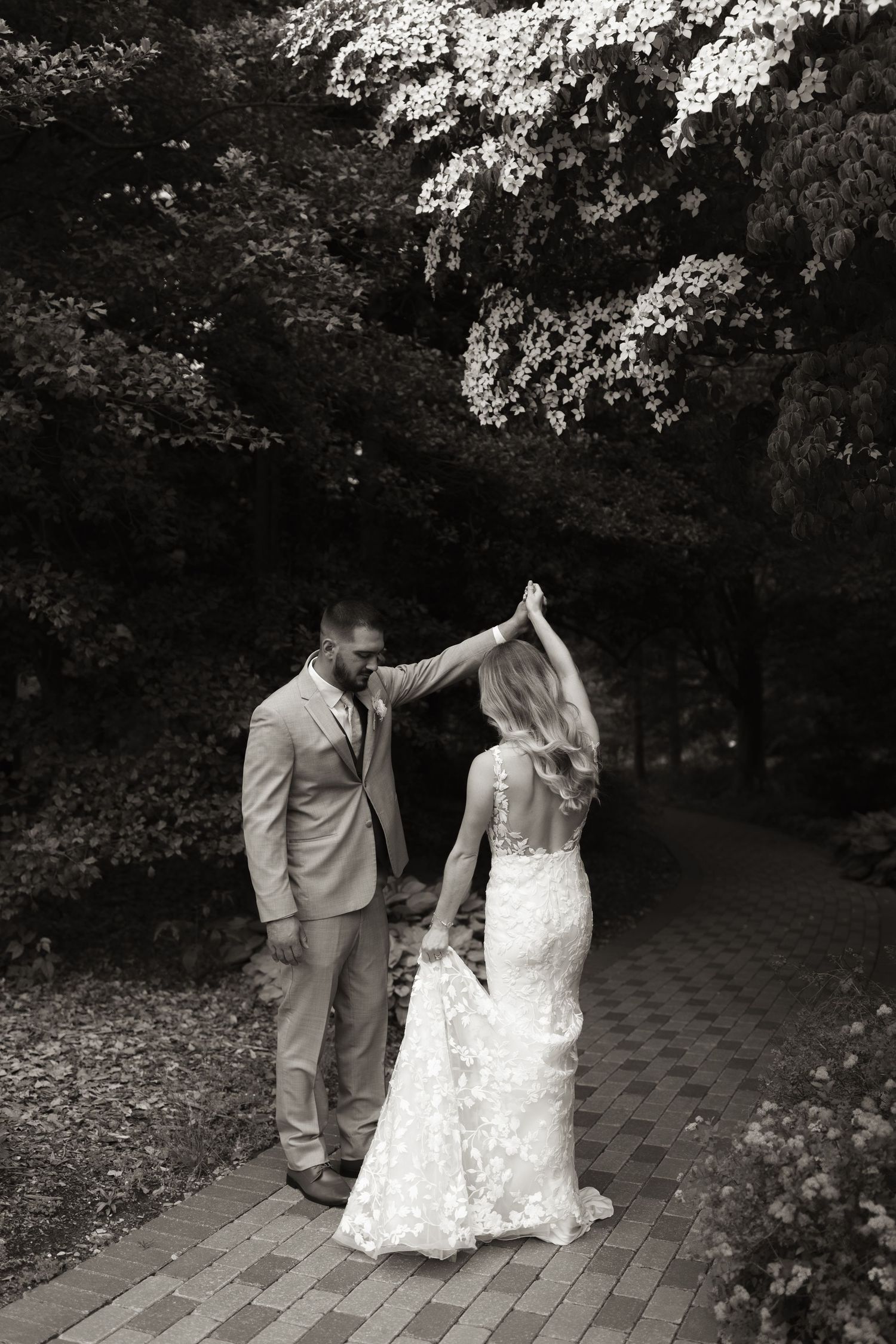 A couple dancing on a brick path surrounded by blooming trees in black and white.