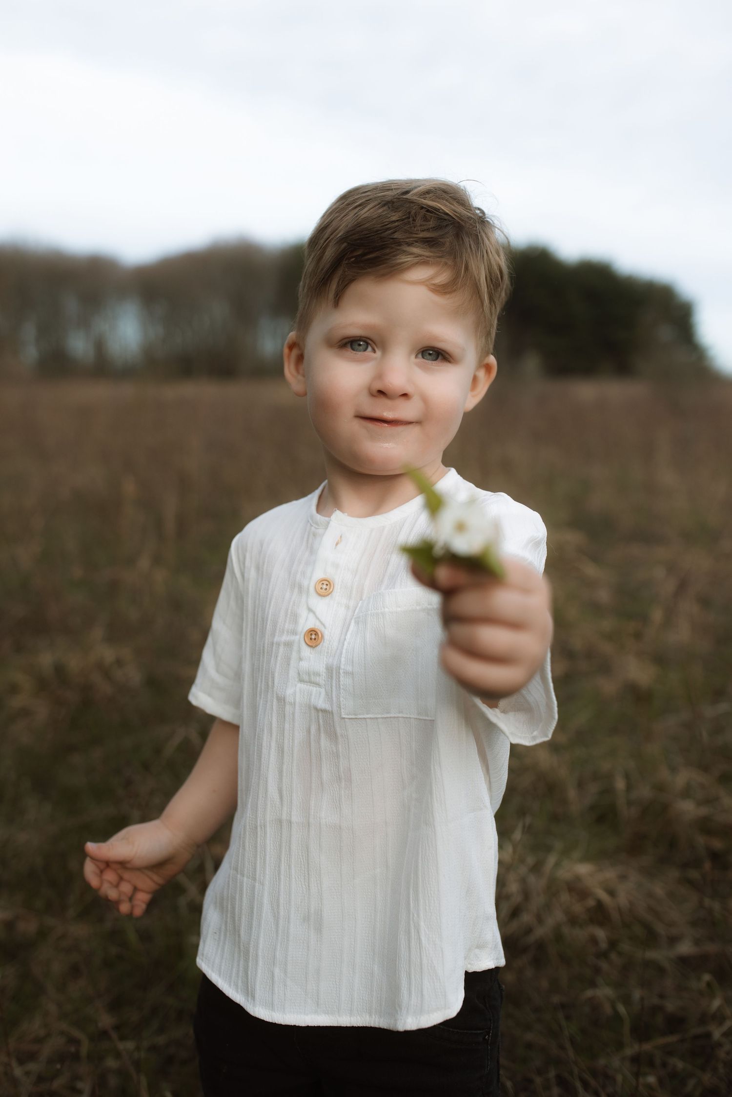 A child in a white button-up shirt holding small white flowers in a field.