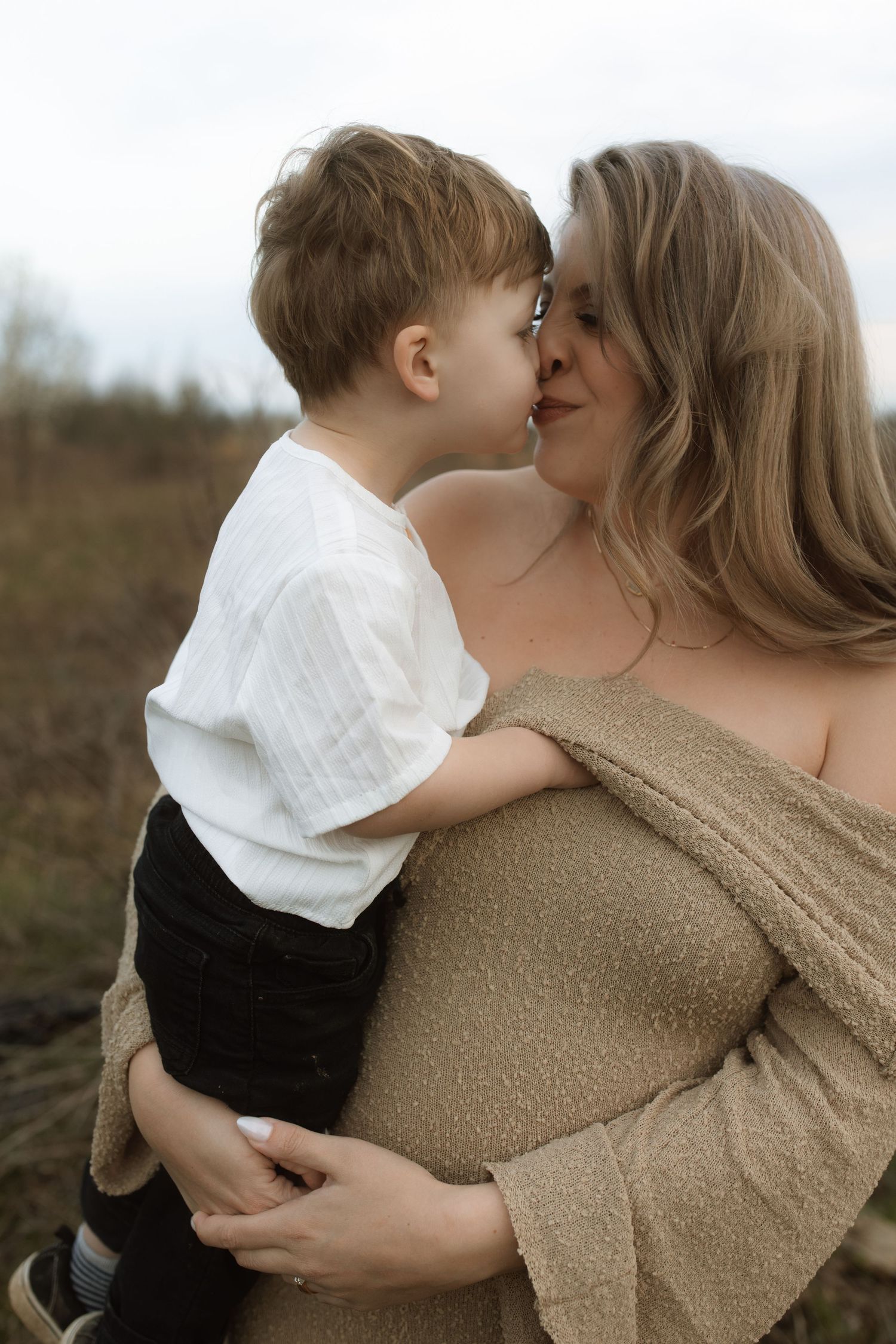 Intimate maternal moment captured outdoors in soft natural lighting.