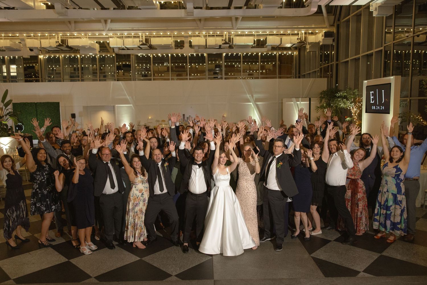 Large group wedding photo with everyone raising hands in celebration on dance floor.