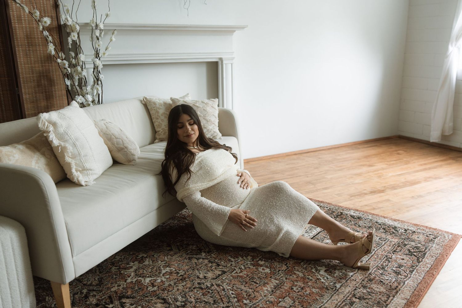 Cozy maternity scene in a minimalist living room with white sofa, hardwood floors and ornate area rug.
