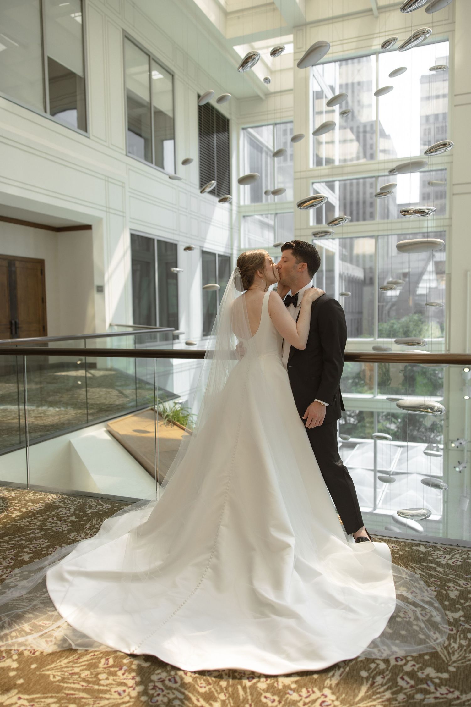 Elegant wedding couple embracing in a modern atrium with glass walls and natural light.