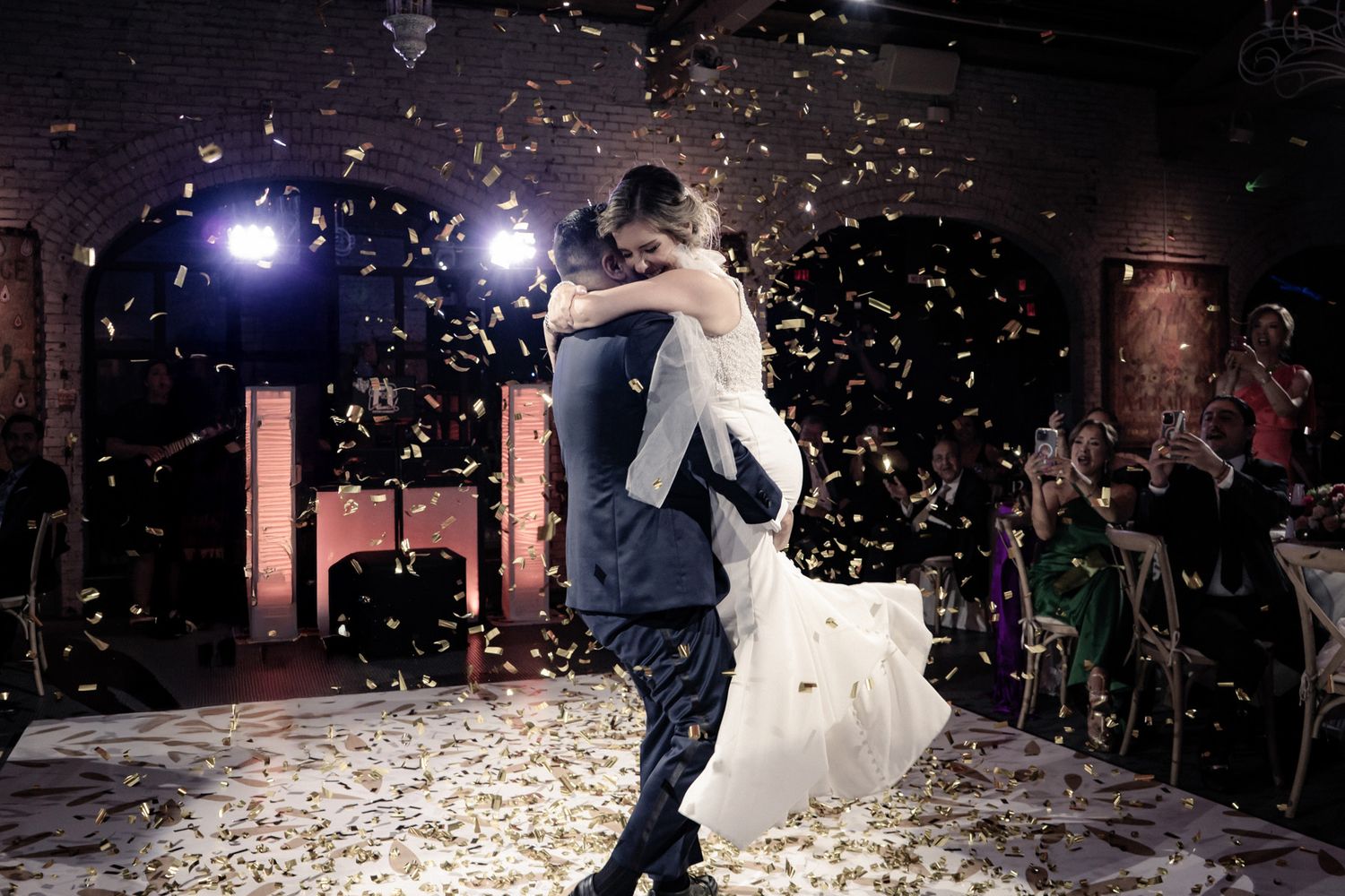 Newlyweds share their first dance surrounded by sparklers on a dark dance floor.