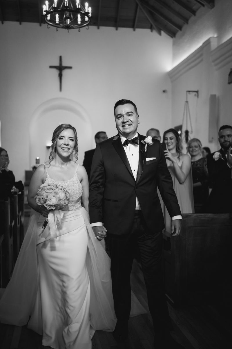 Newlyweds exit their church ceremony while guests applaud in this black and white moment.