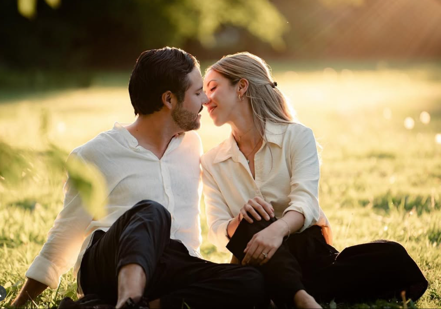 Romantic couple sitting close together in sunlit meadow during golden hour.