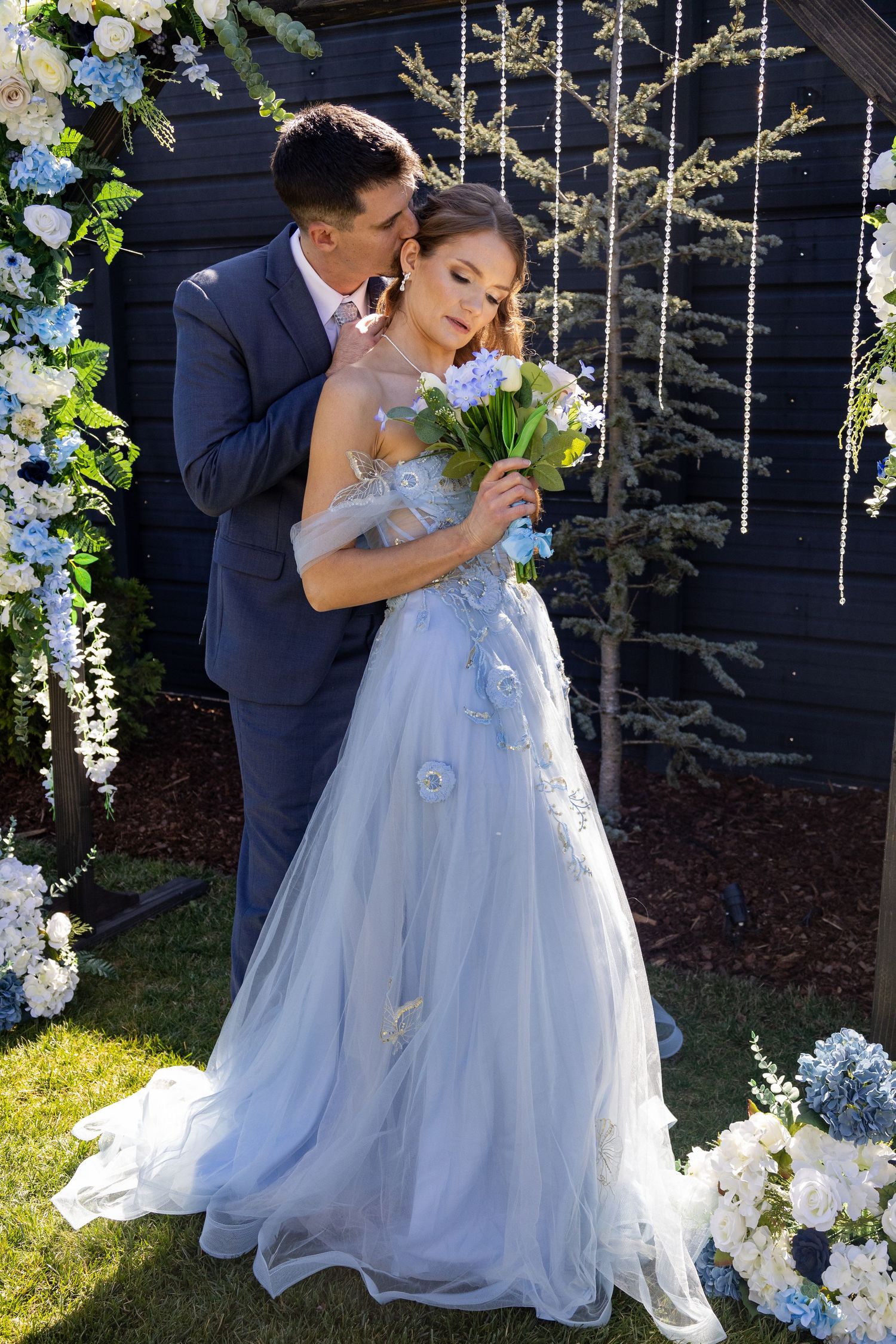A romantic wedding portrait of a couple embracing among blue and white floral decorations.