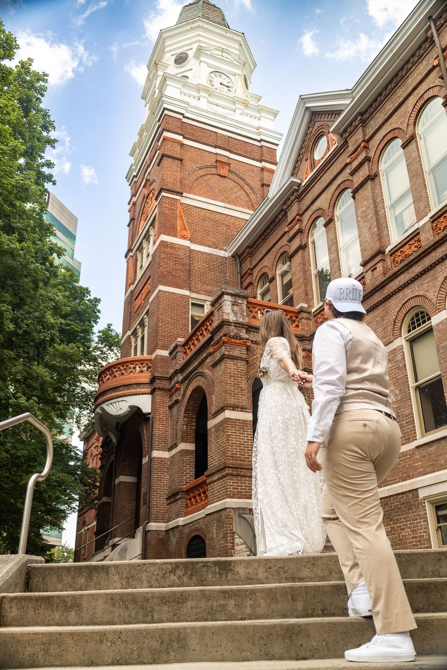 Historic red brick bell tower stands tall above concrete steps leading to a Victorian-style courthouse building.