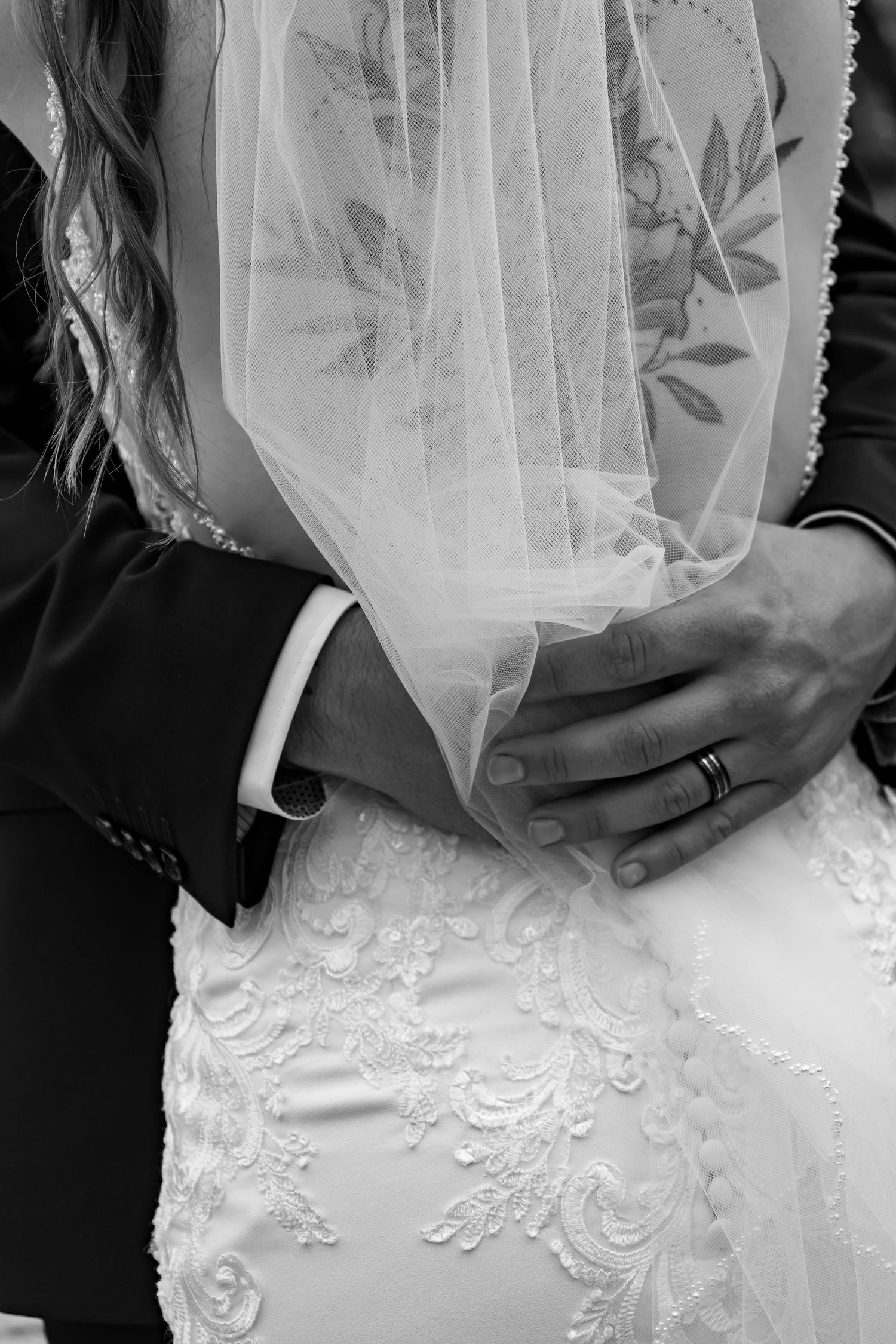 Black and white close-up of a wedding couple embracing, showing detailed lace dress and veil details.