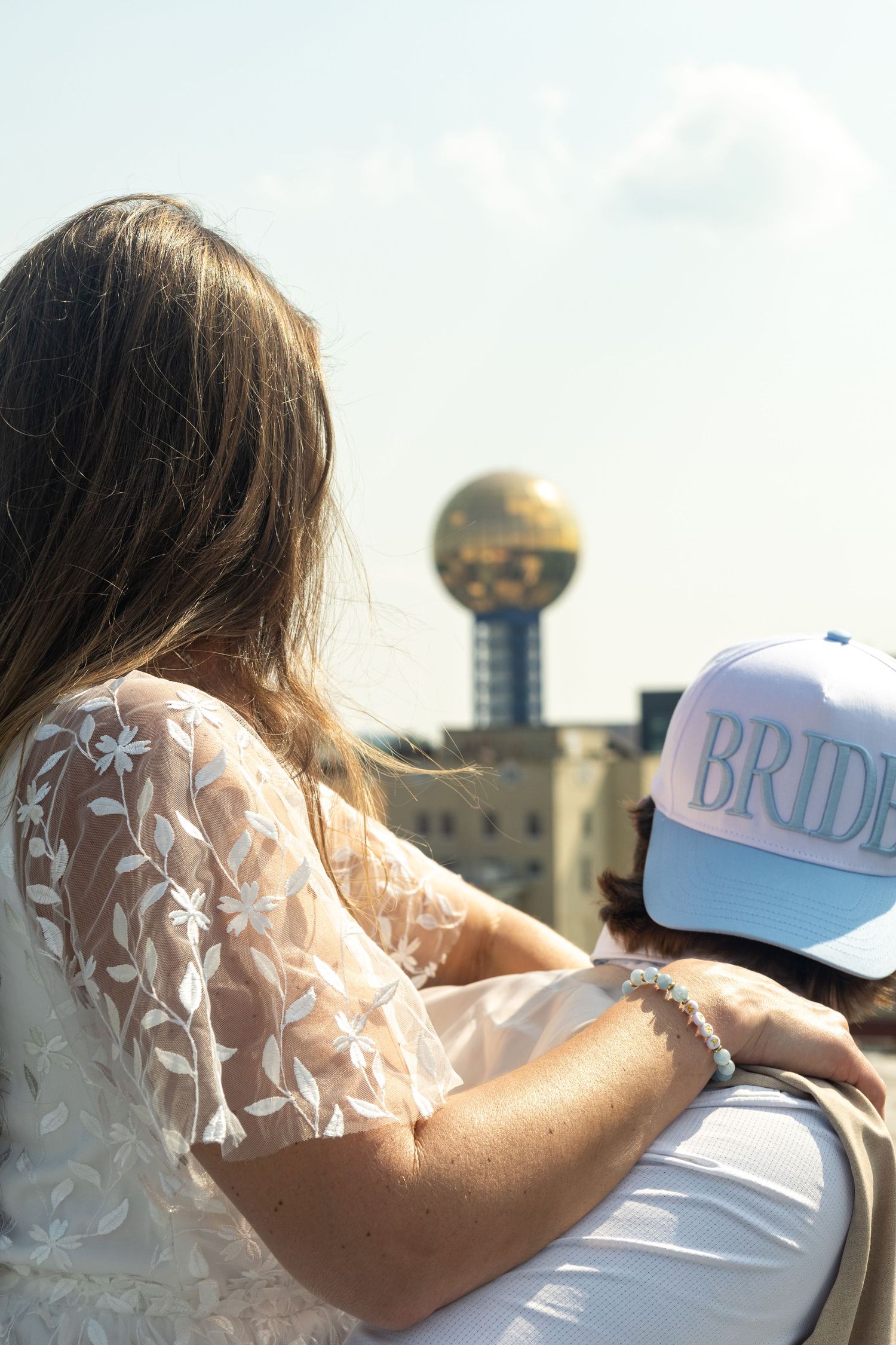 Decorative white bridal attire and cap visible against an industrial backdrop with a spherical structure in the distance.