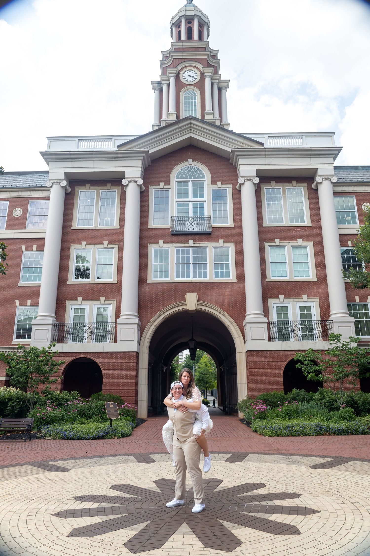 Elegant brick academic building with clock tower and archway entrance featuring circular paver pattern in foreground.