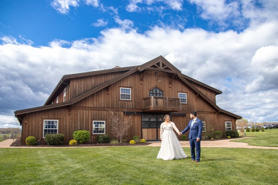 Rustic barn wedding venue with wooden exterior and couple holding hands in foreground.