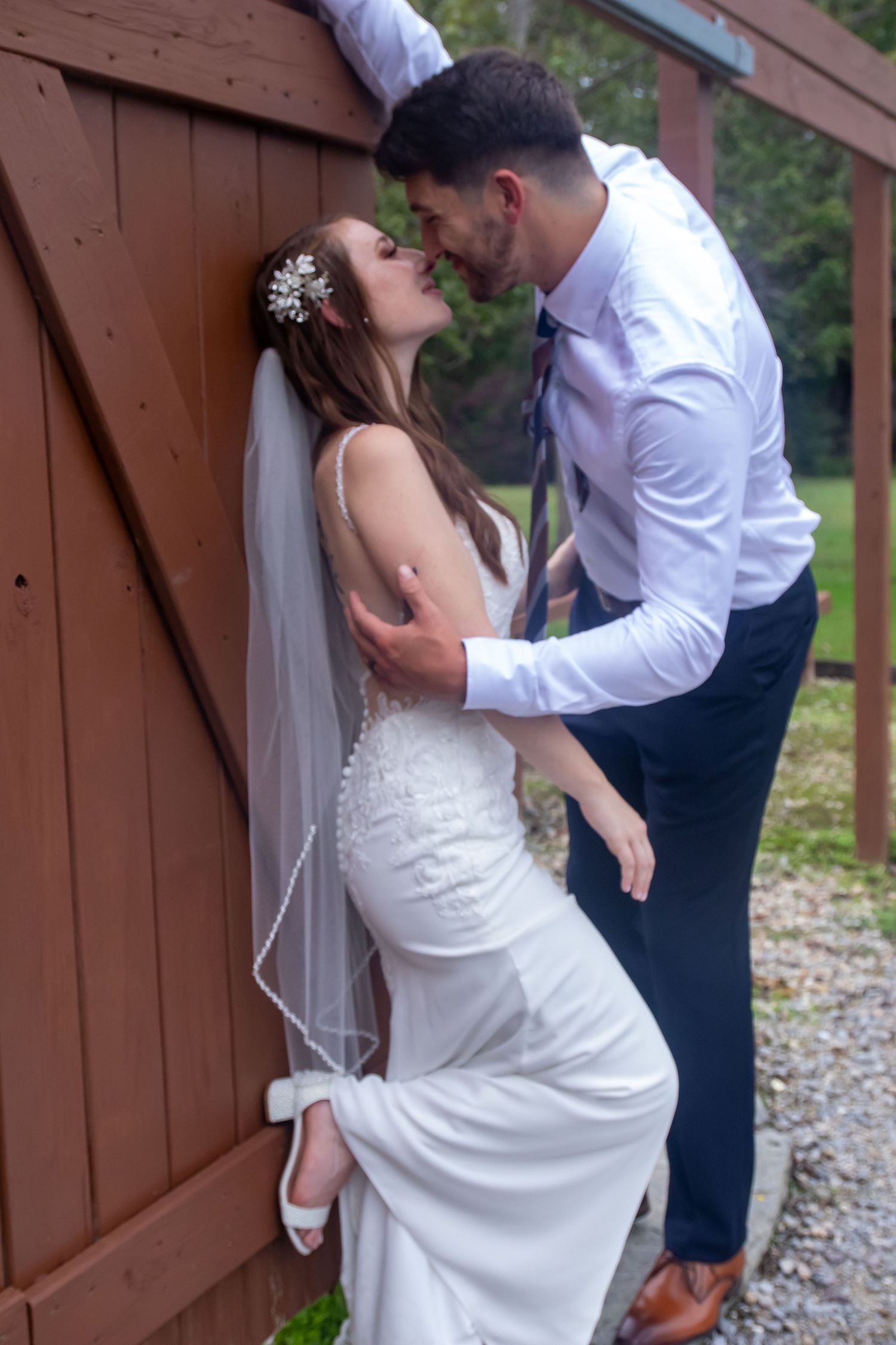 Intimate wedding portrait against red barn door with bride in fitted lace gown.