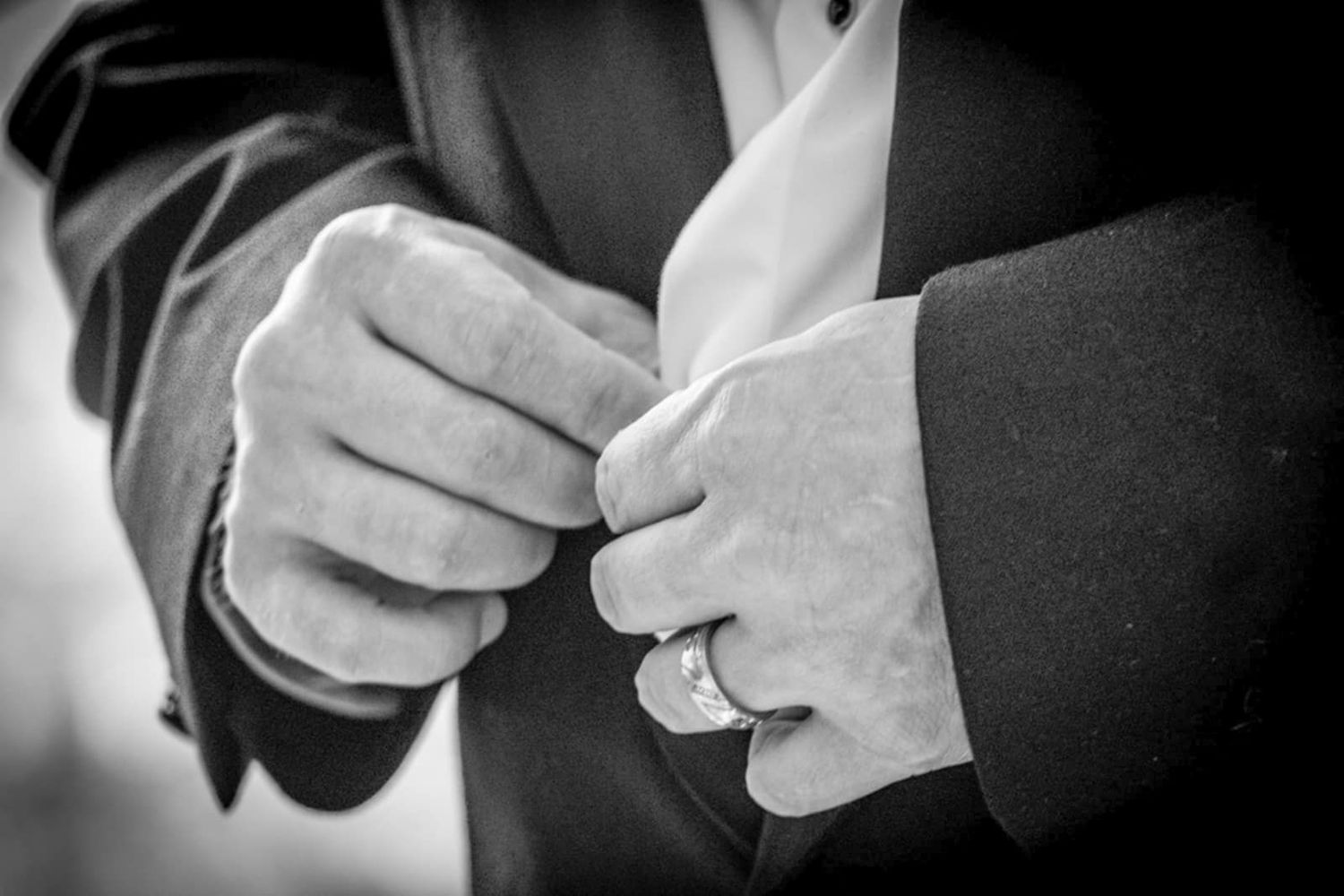 Close-up black and white photo of hands exchanging wedding rings during a ceremony.