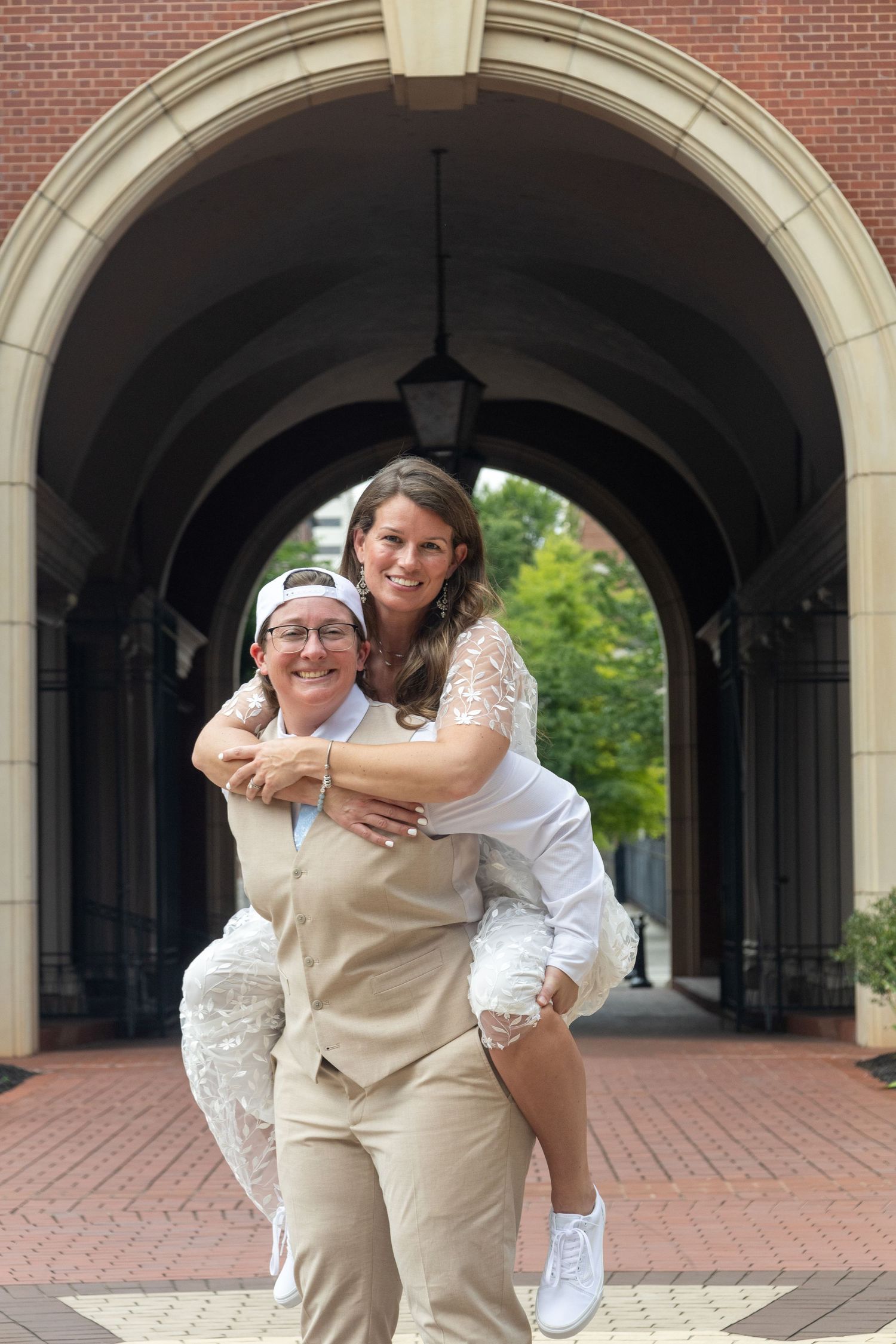 A joyful piggyback ride moment captured under a brick archway on a university campus.