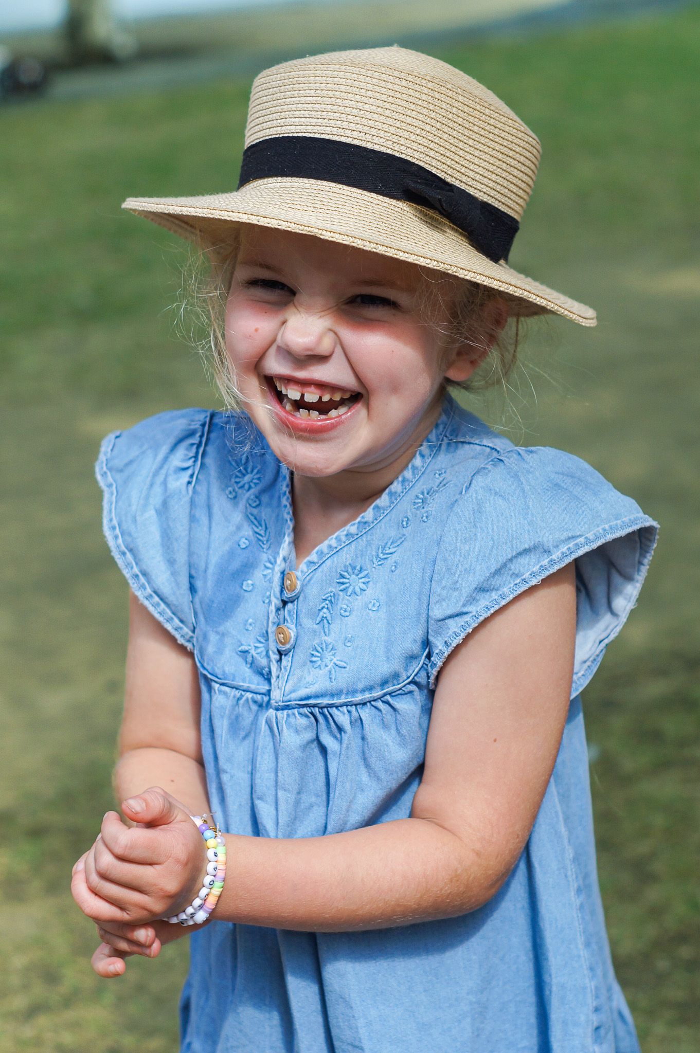 A joyful moment captured outdoors showing a light blue dress and straw hat with black band on a sunny day.