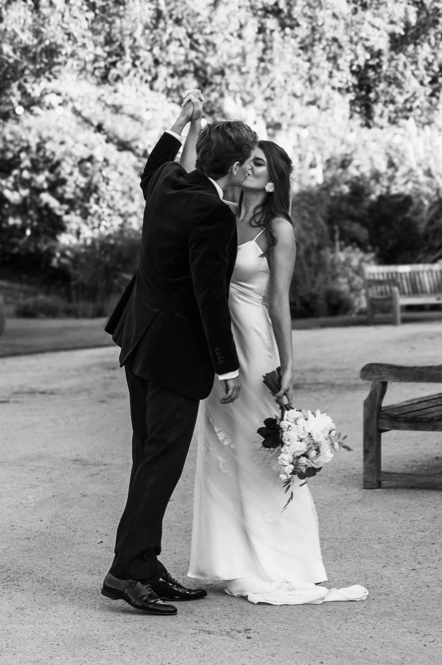 A couple shares an intimate black and white wedding moment outdoors, with the bride holding a floral bouquet.