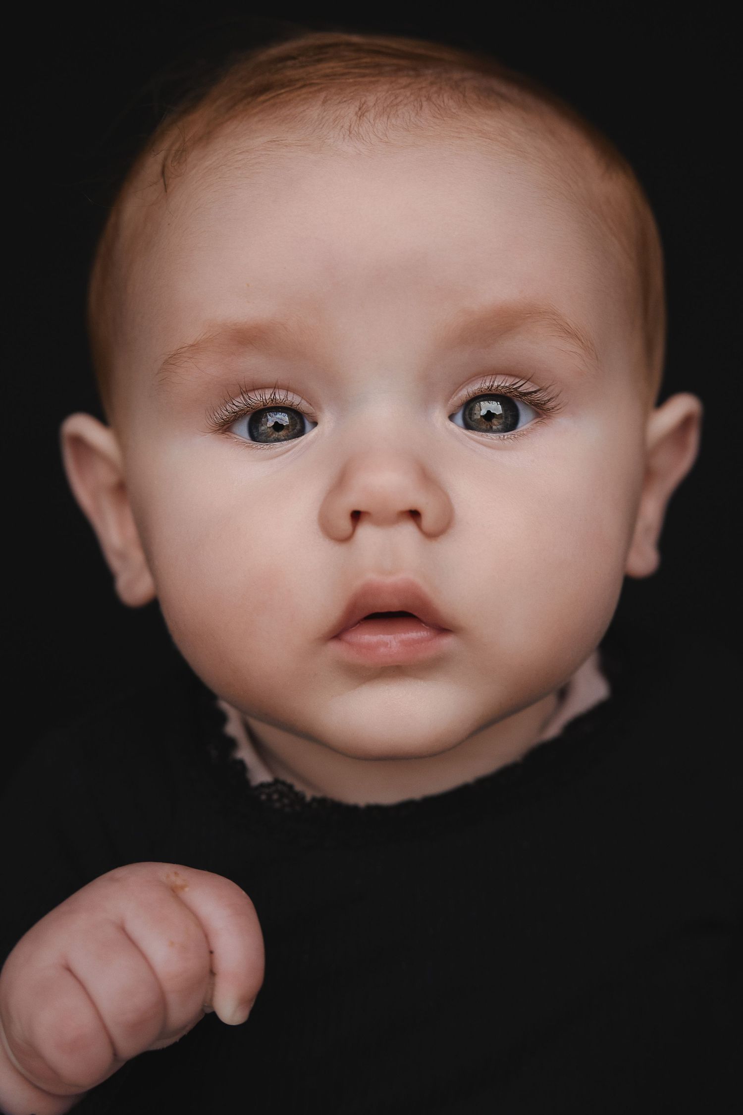 Close-up portrait of a baby with wide brown eyes against a dark background.