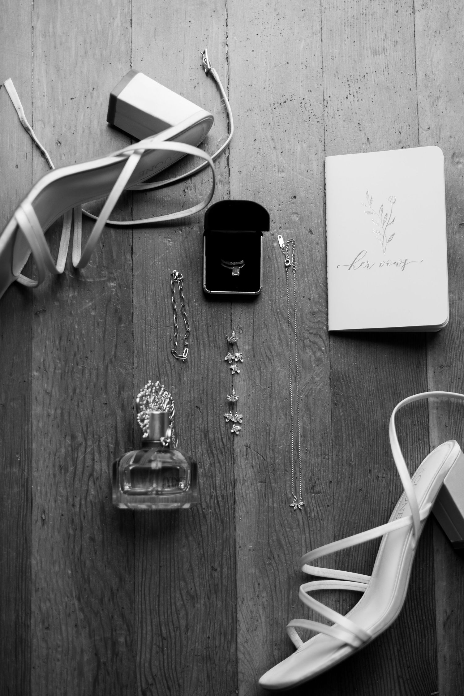 Wedding accessories flatlay including white heels, jewelry, and ring box on wooden surface.