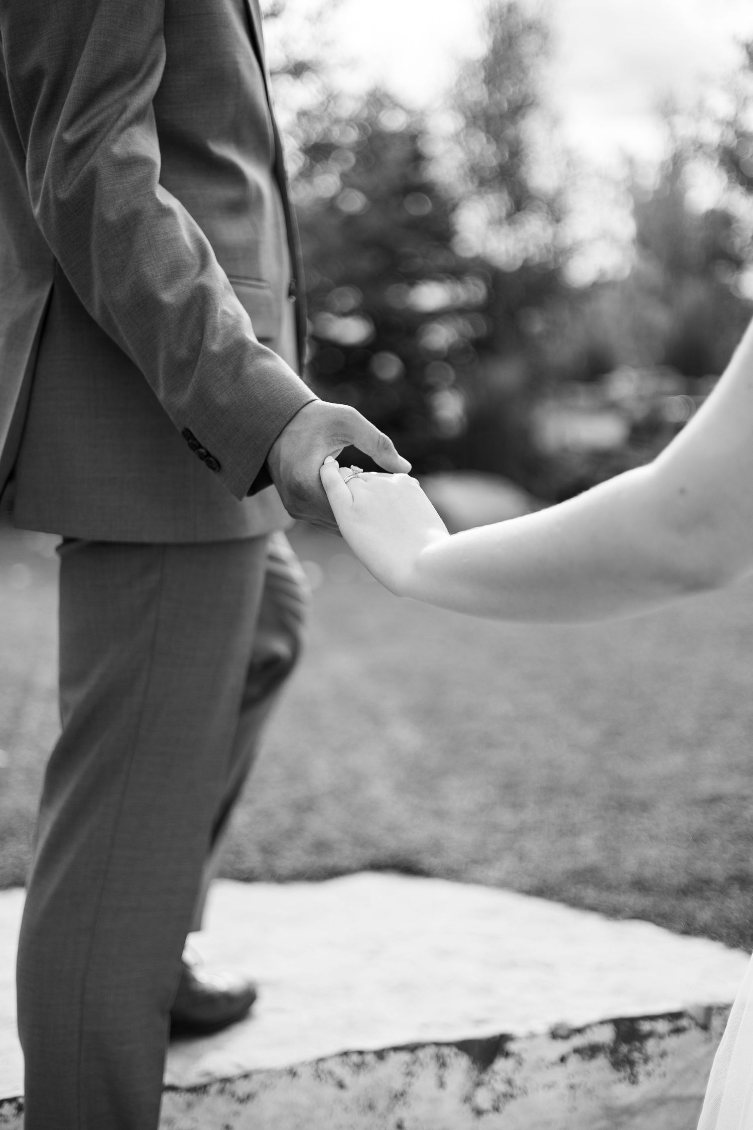 A black and white photo of hands tenderly touching during a wedding ceremony.
