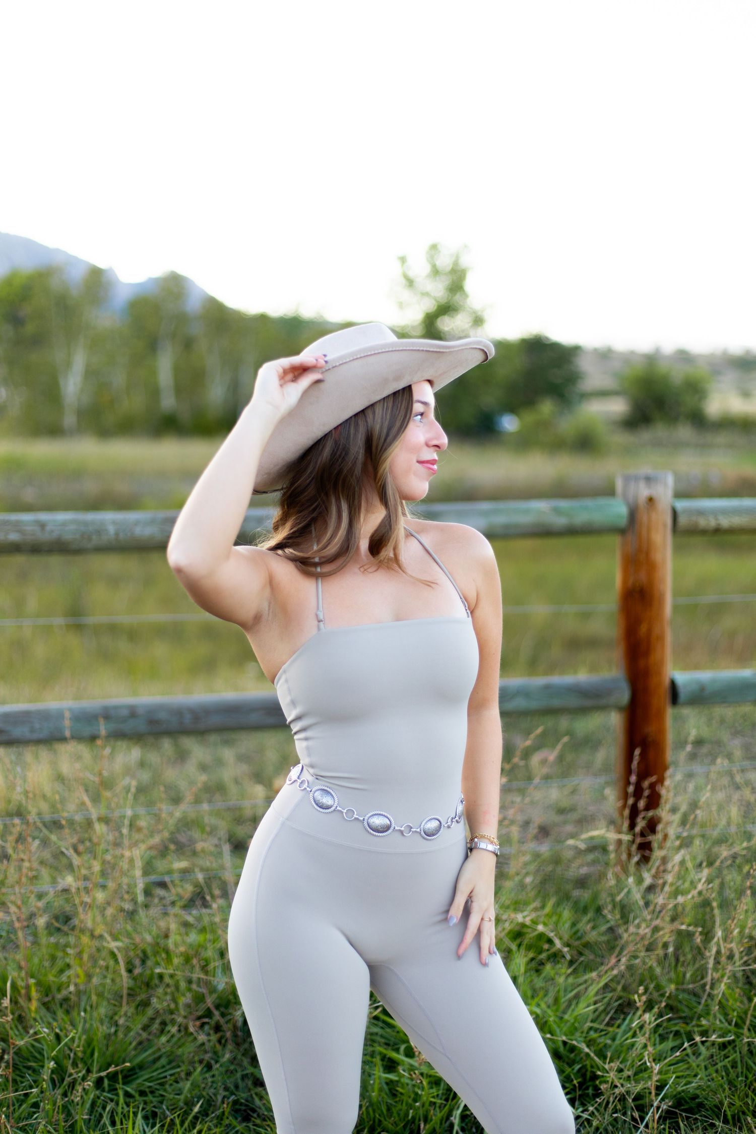 Woman in athletic wear and hat poses by wooden fence in mountain setting.