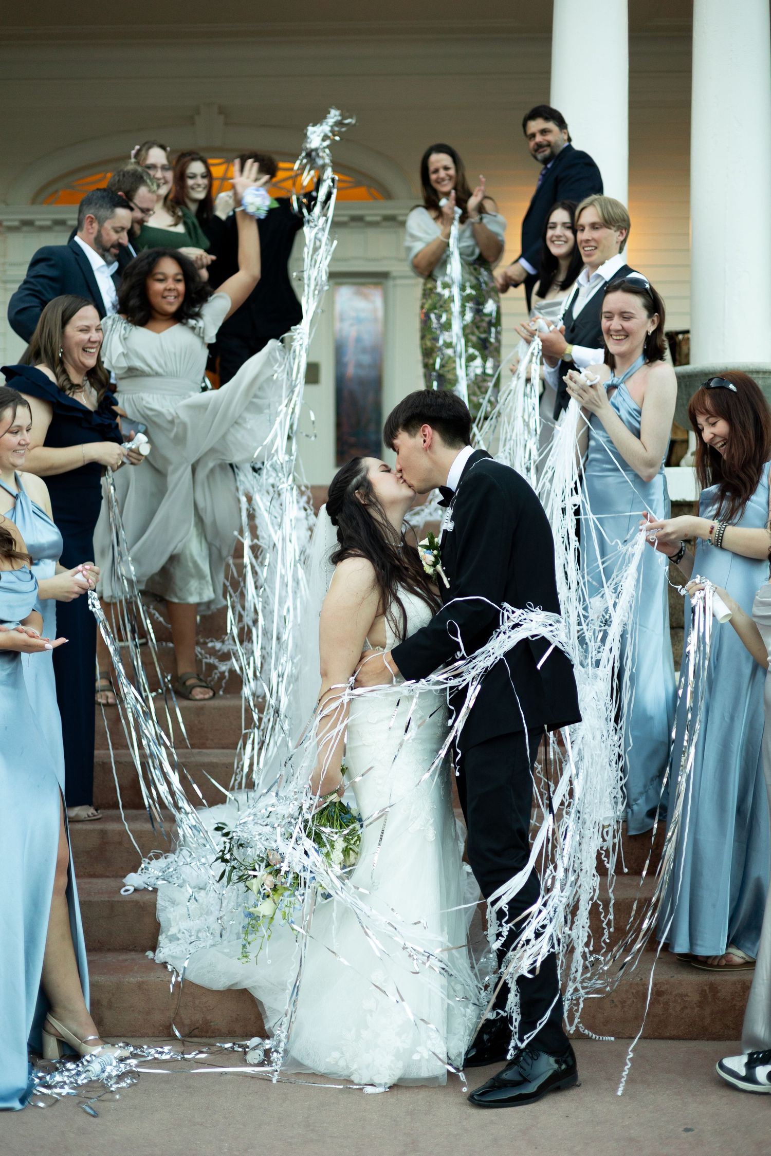 Wedding party members spray silly string at each other during a fun celebratory moment in formal attire.