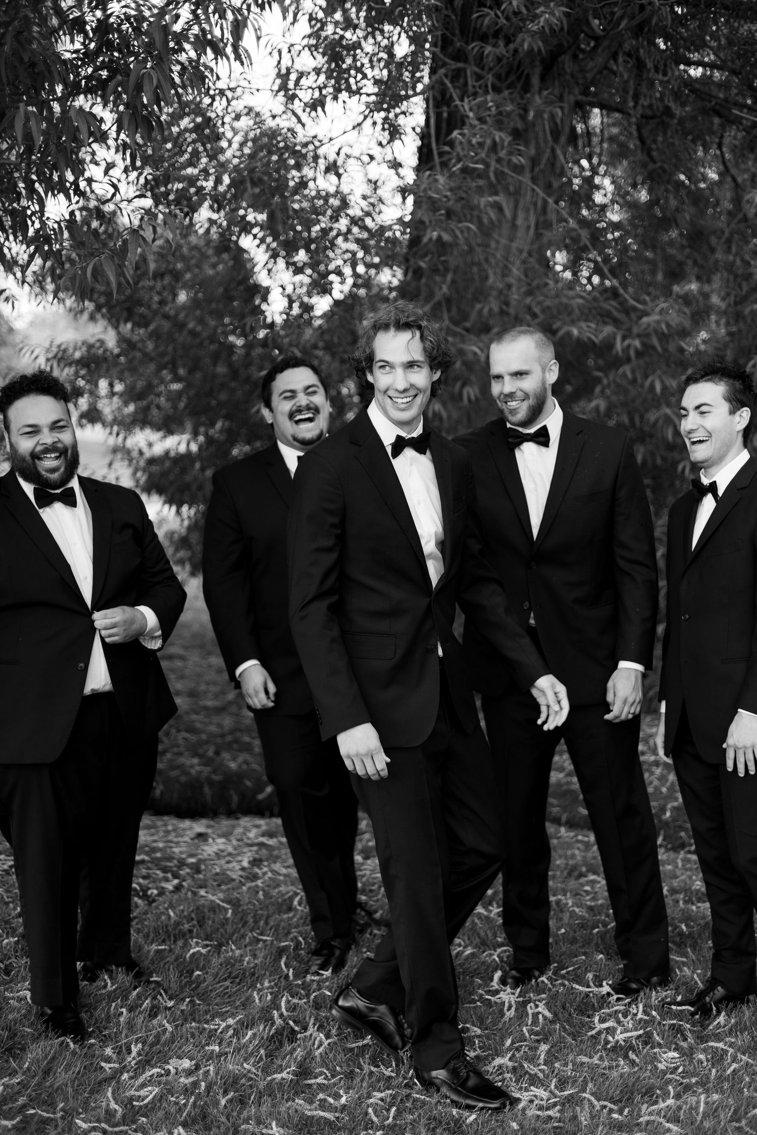 Groomsmen in tuxedos share a candid laughing moment during wedding photos.