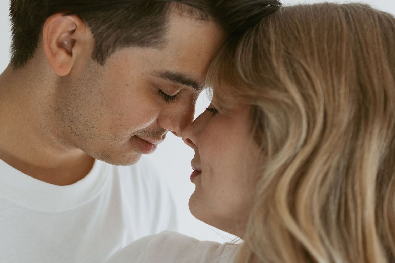 Romantic couple in white shirts share intimate moment touching foreheads.