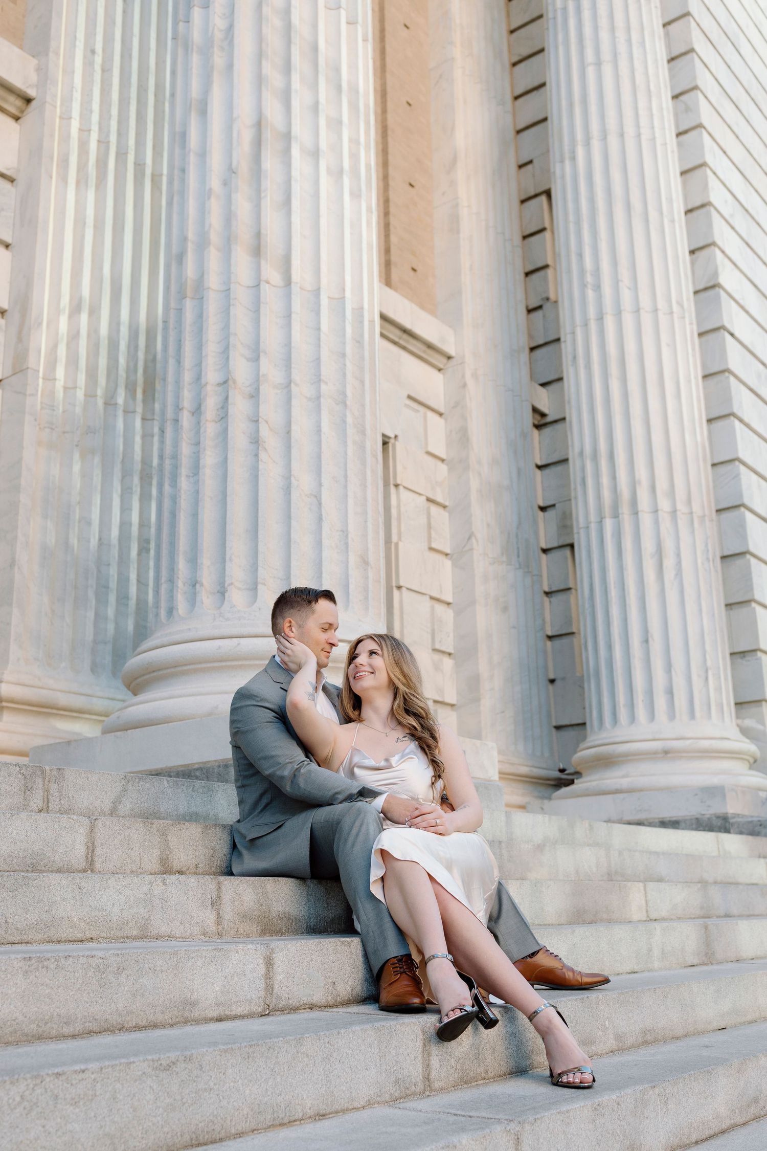 Romantic couple in formal wear poses on classical building steps with grand columns.