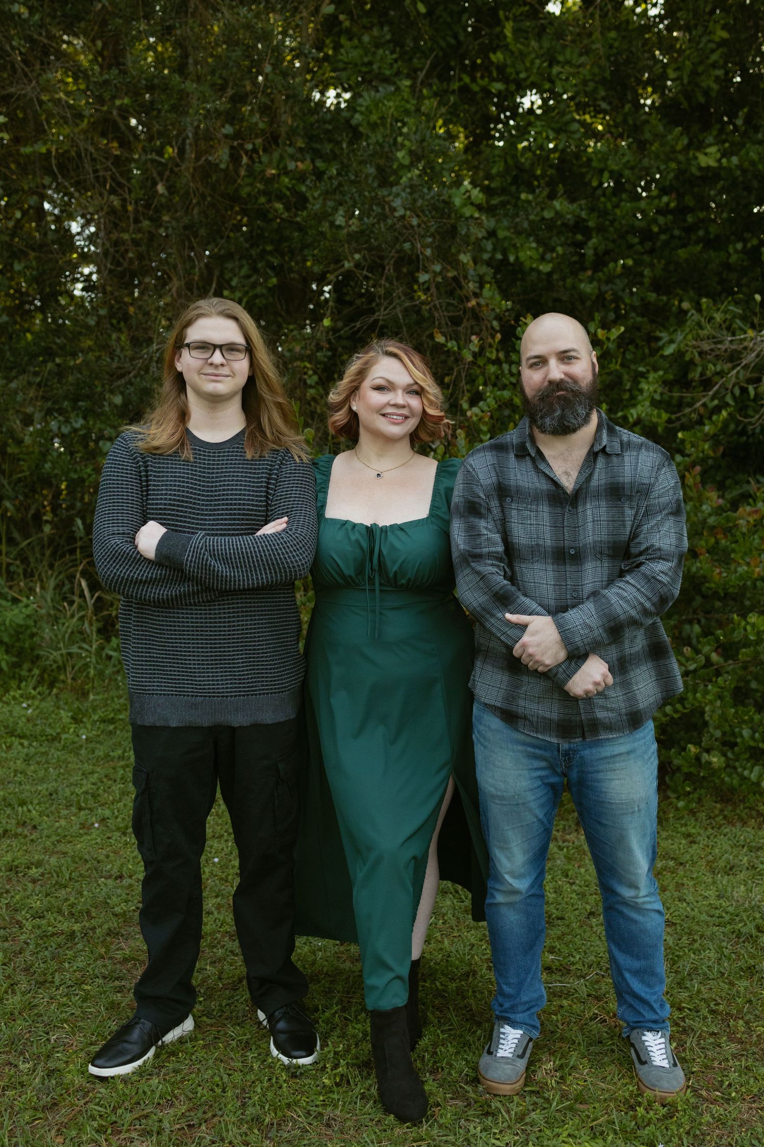 Three people pose together outdoors, with greenery in background.