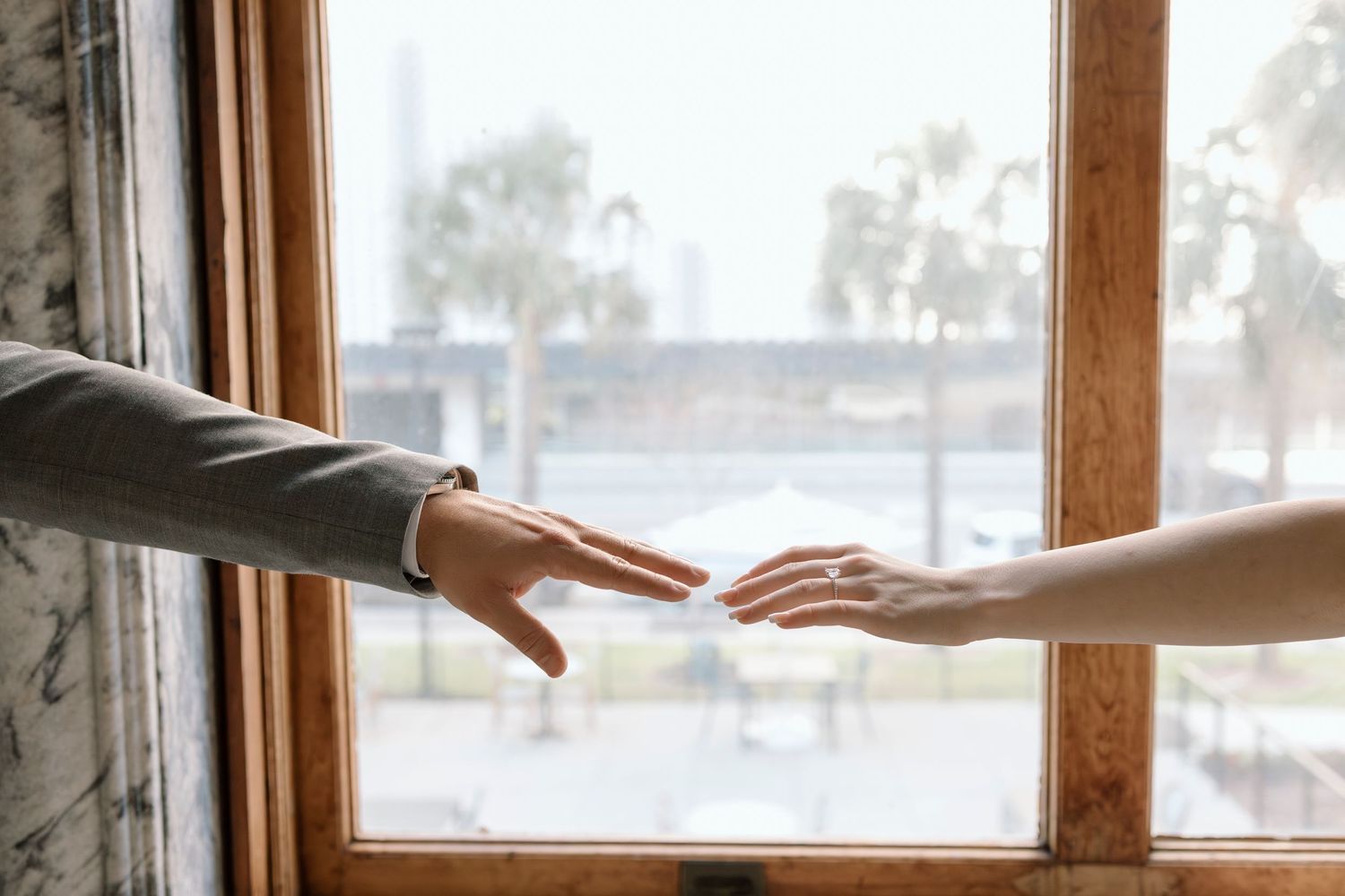 Two hands reaching toward each other in front of window with palms visible in background.